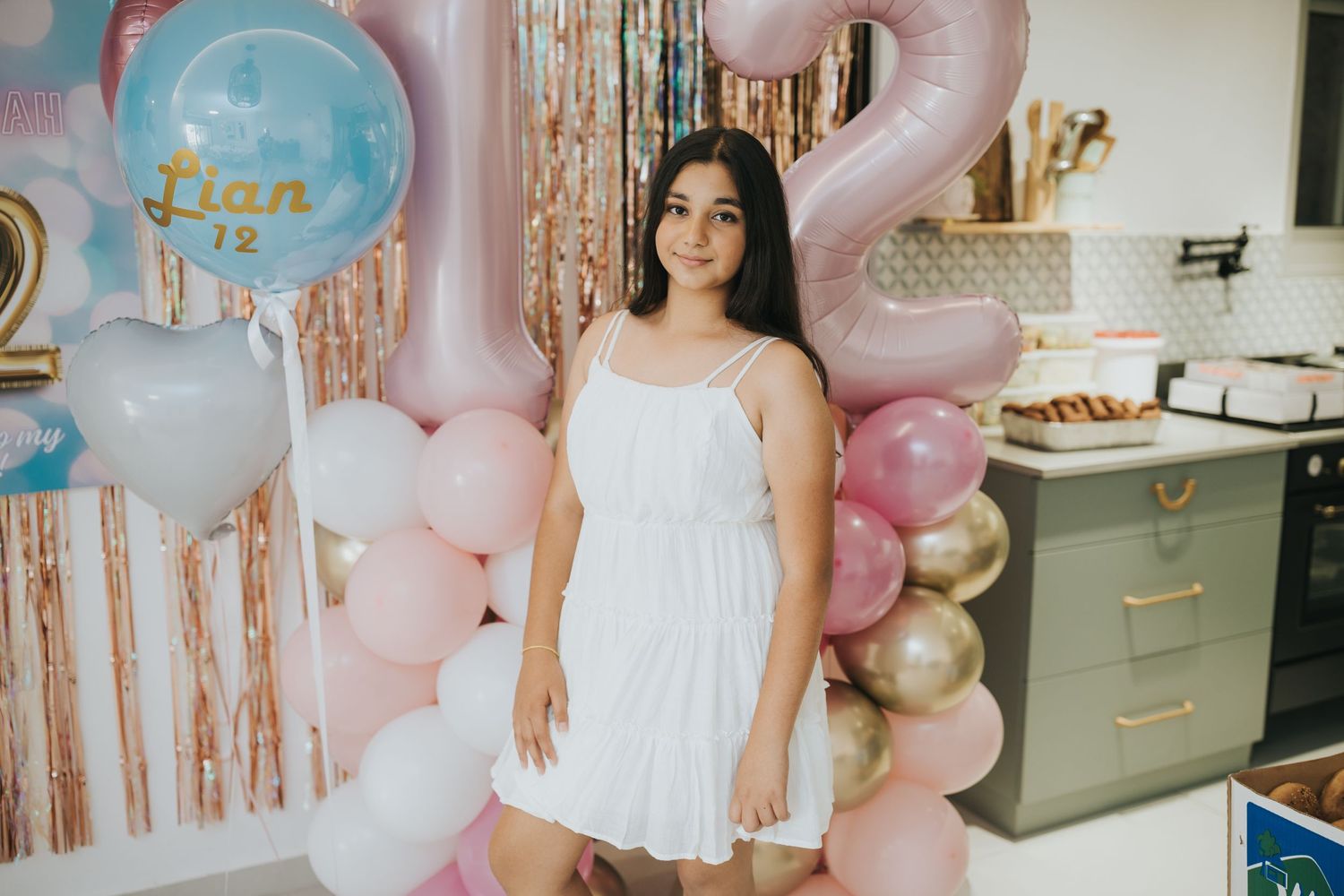 White dress against pink and gold balloon backdrop at celebration.
