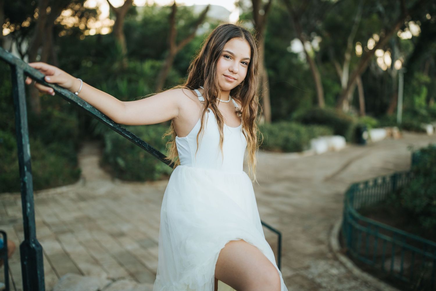 Woman in flowing white dress poses gracefully on outdoor steps at sunset.