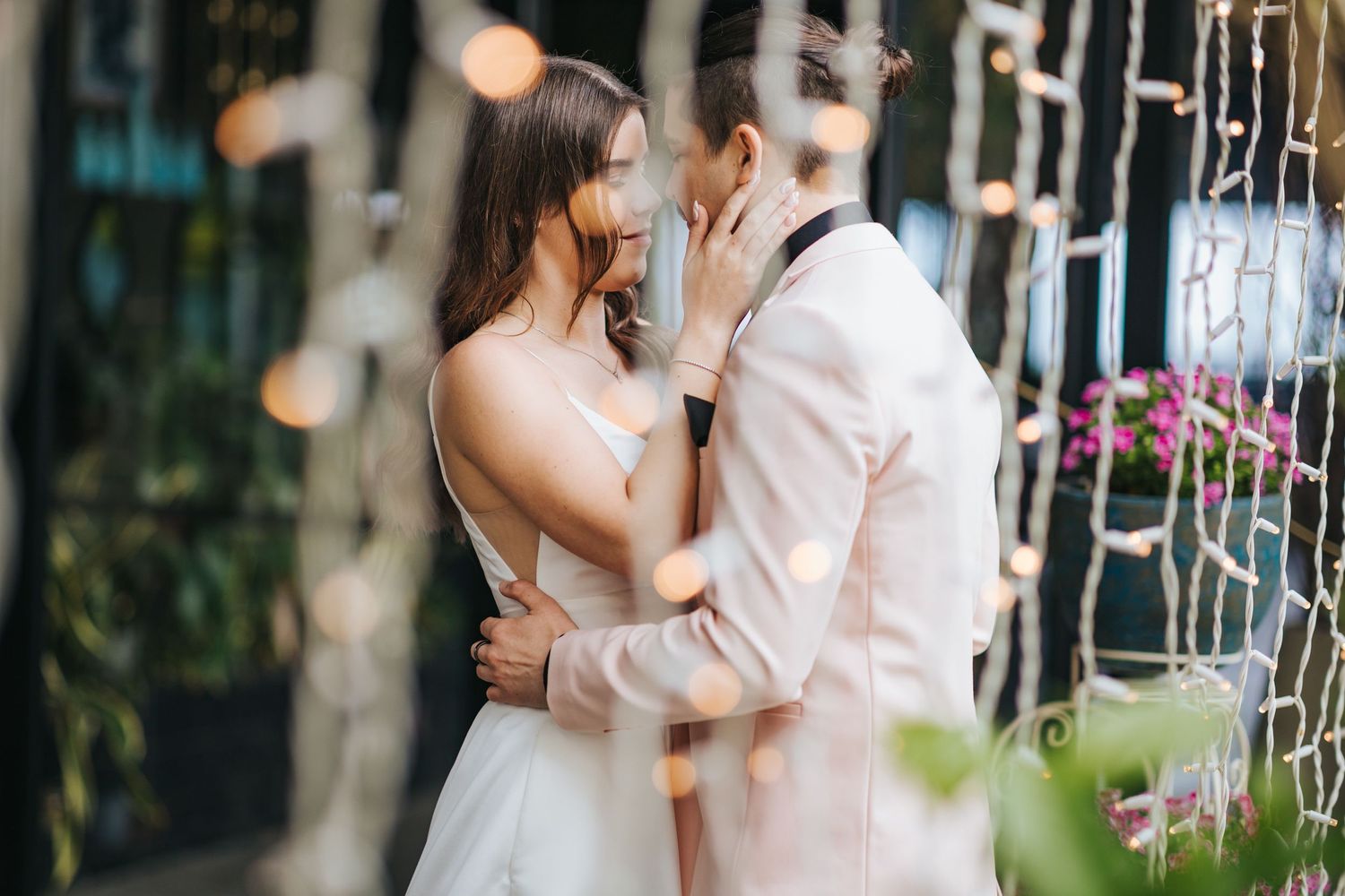 Intimate moment between newlyweds surrounded by string lights and greenery.