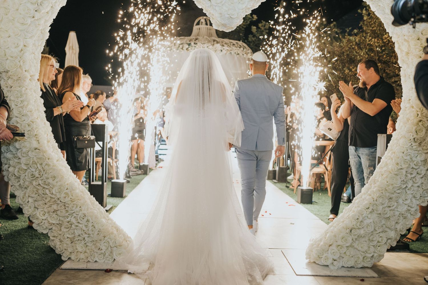 Wedding ceremony under floral heart arch with guests watching from sides.