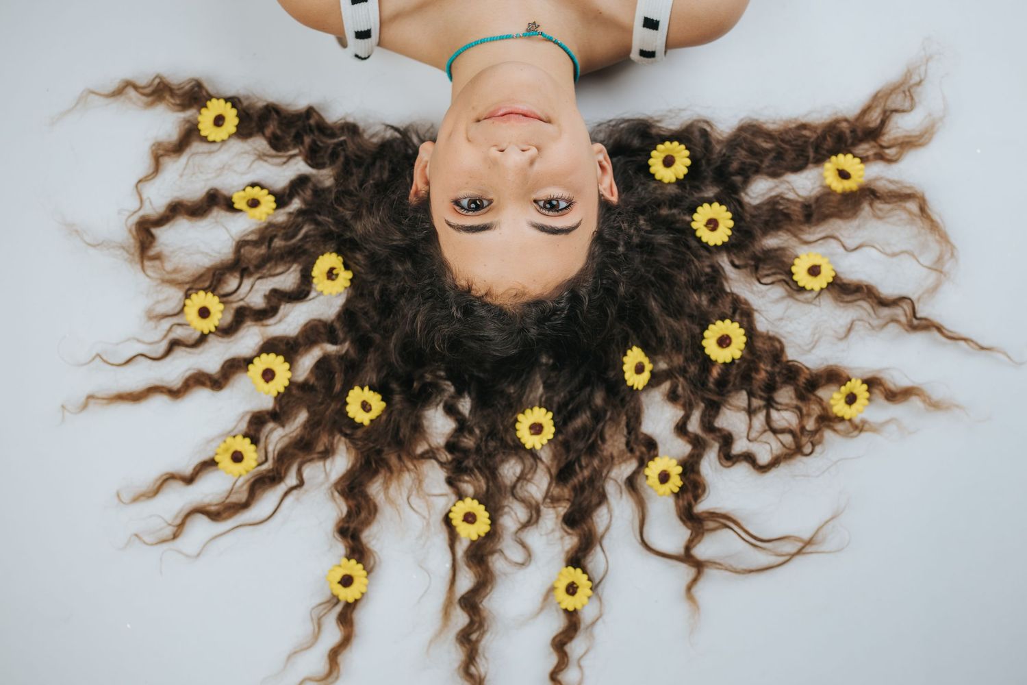 Creative portrait with long curly hair spread out with sunflowers arranged in a circular pattern.