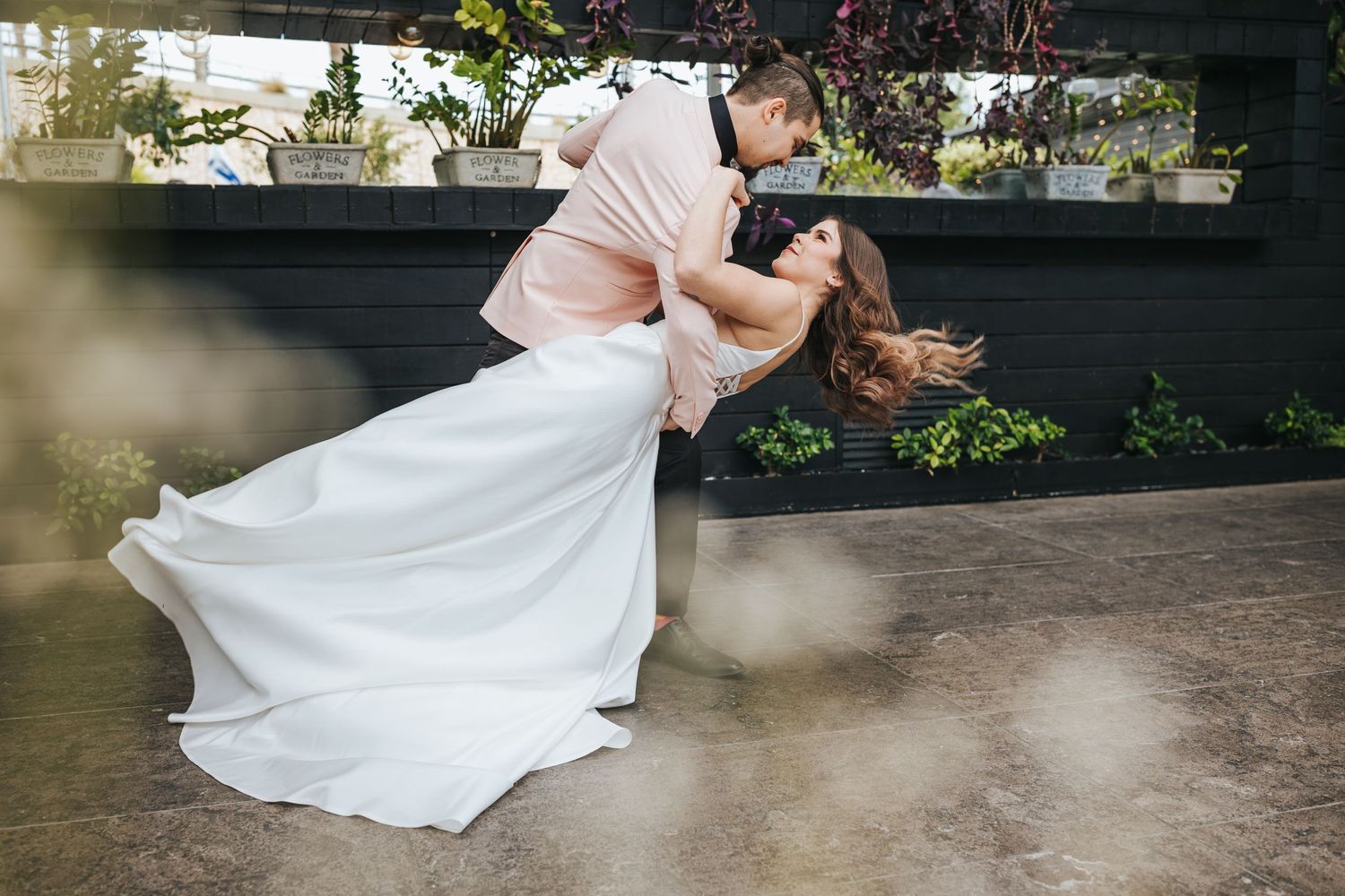 Dramatic dip pose between newlyweds in white dress and pink suit outdoors.