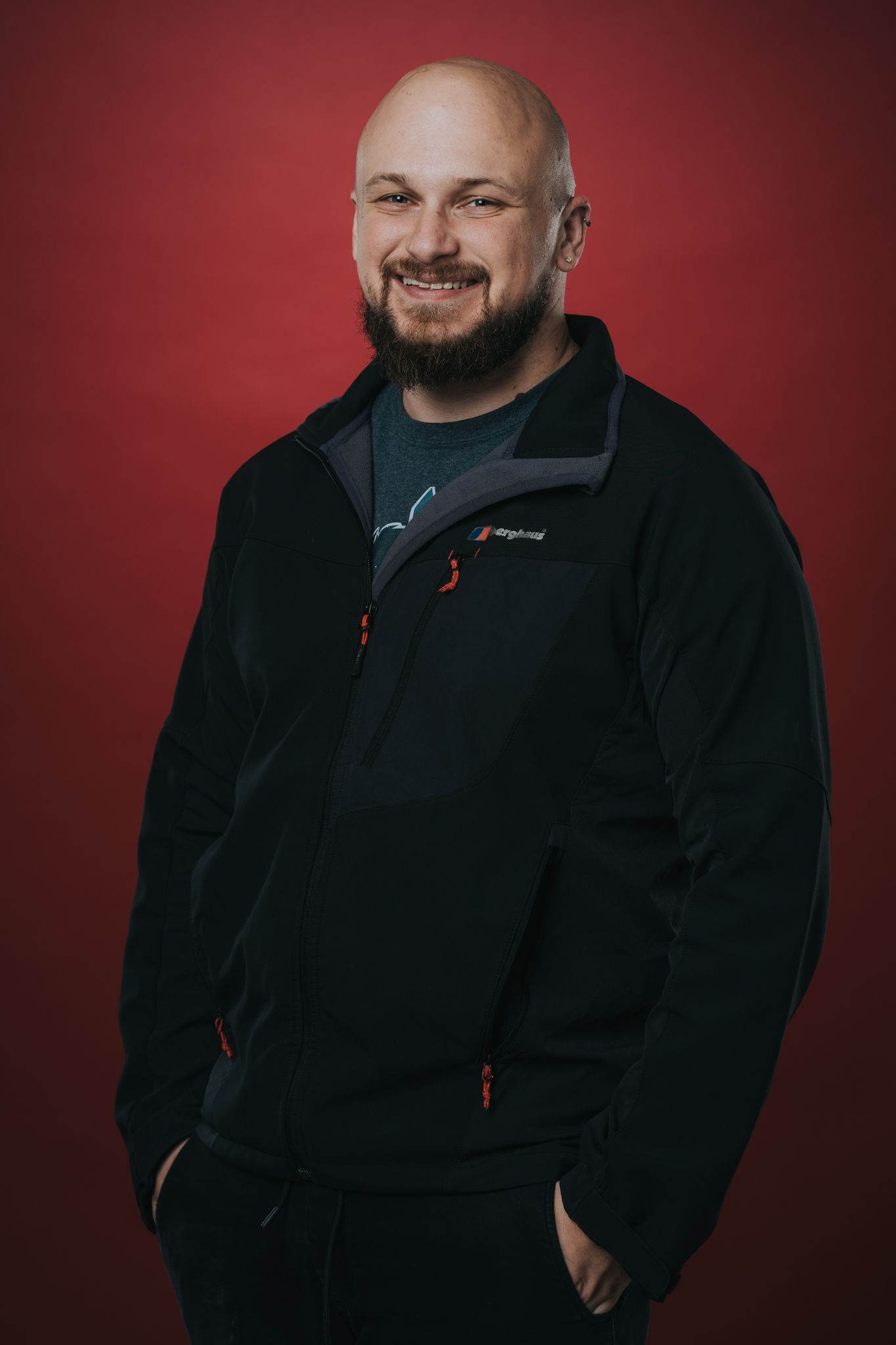Professional portrait of person in black fleece jacket against red background.