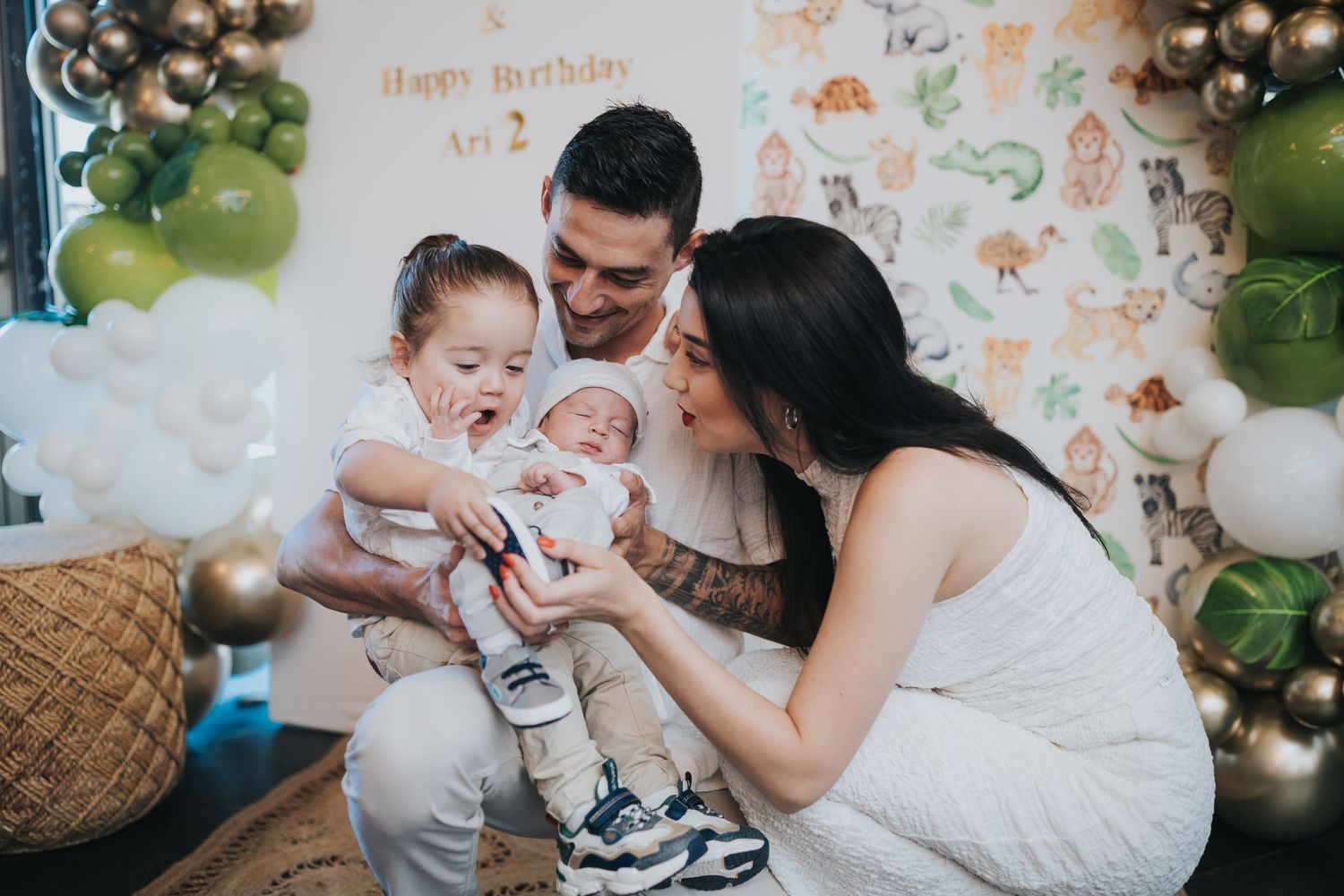 Family gathering around a newborn with balloon decorations and safari-themed backdrop.