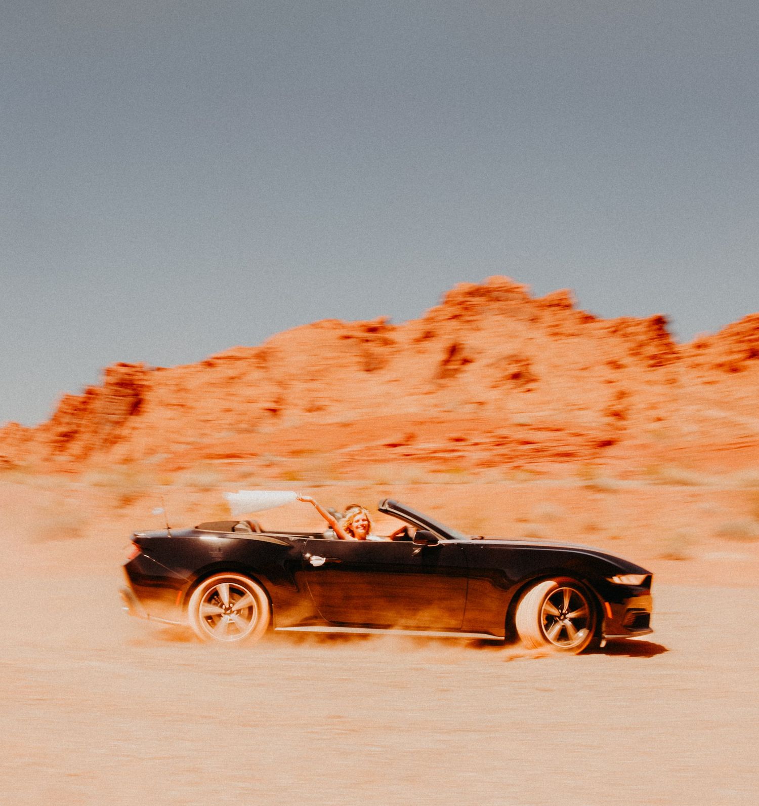 Bride holding her veil in a mustang in the desert during destination wedding in Nevada, USA.