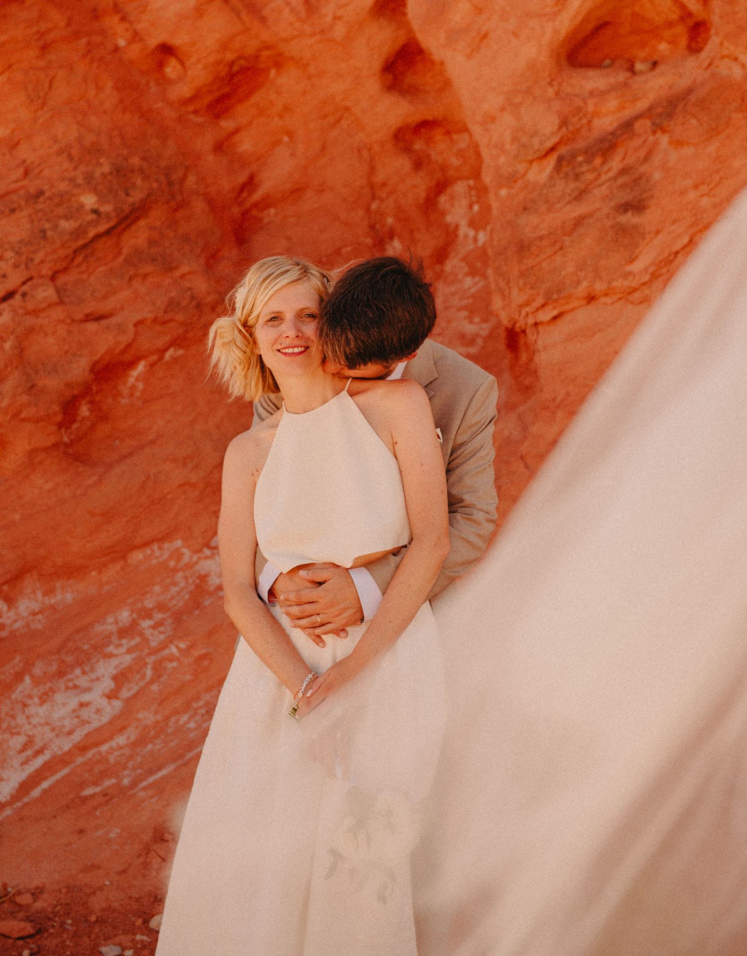Groom kissing bride in front of red rocks during destination wedding in Nevada, USA.