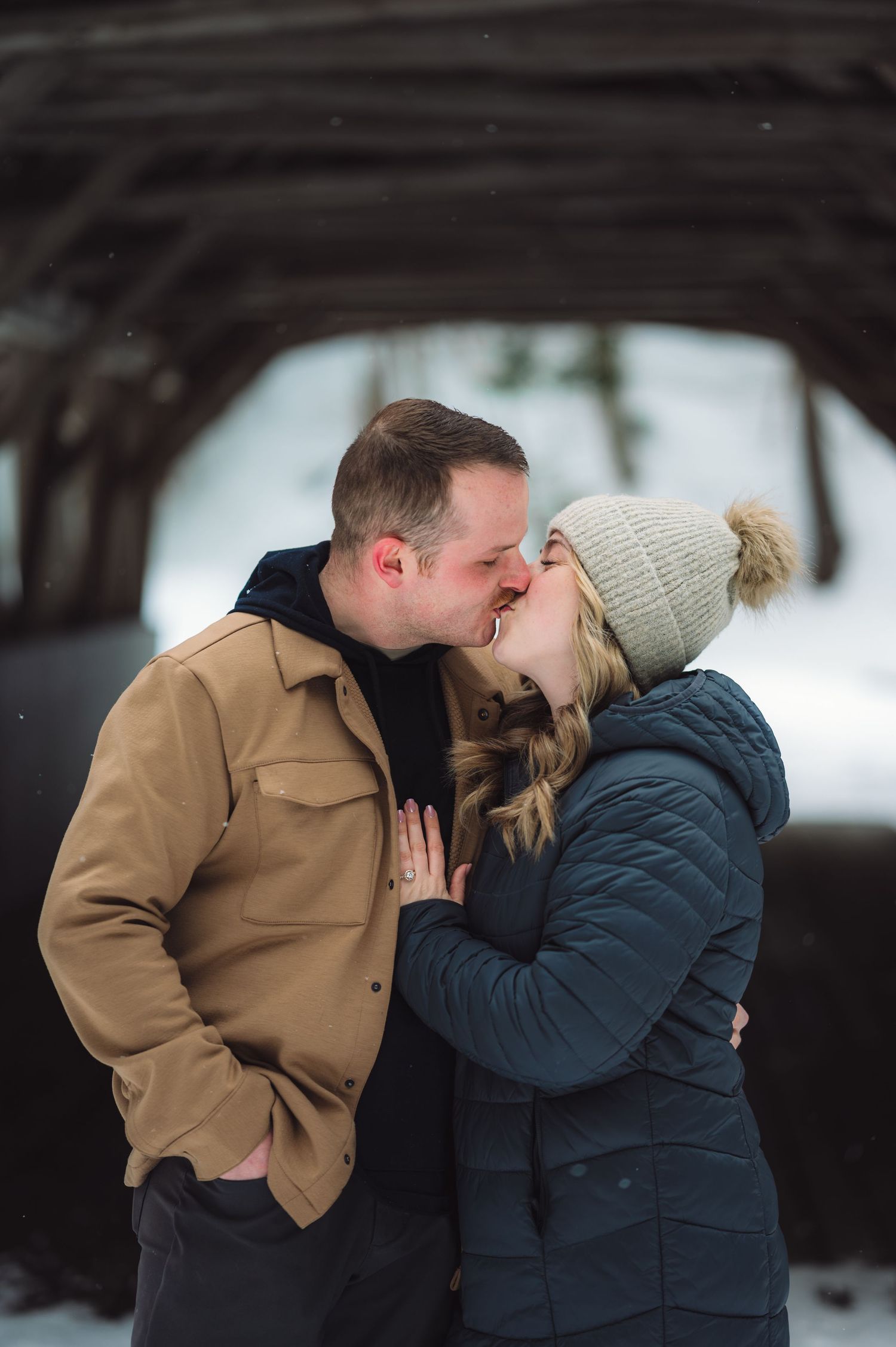A couple shares a romantic kiss outdoors in winter while wearing warm coats and winter accessories.