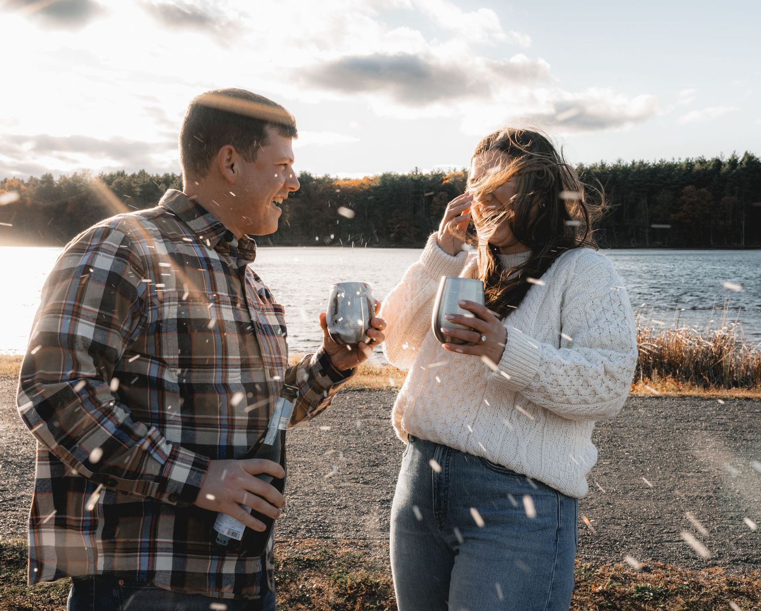 A couple in plaid and denim stands close together while looking at a map by a scenic lake at sunset.