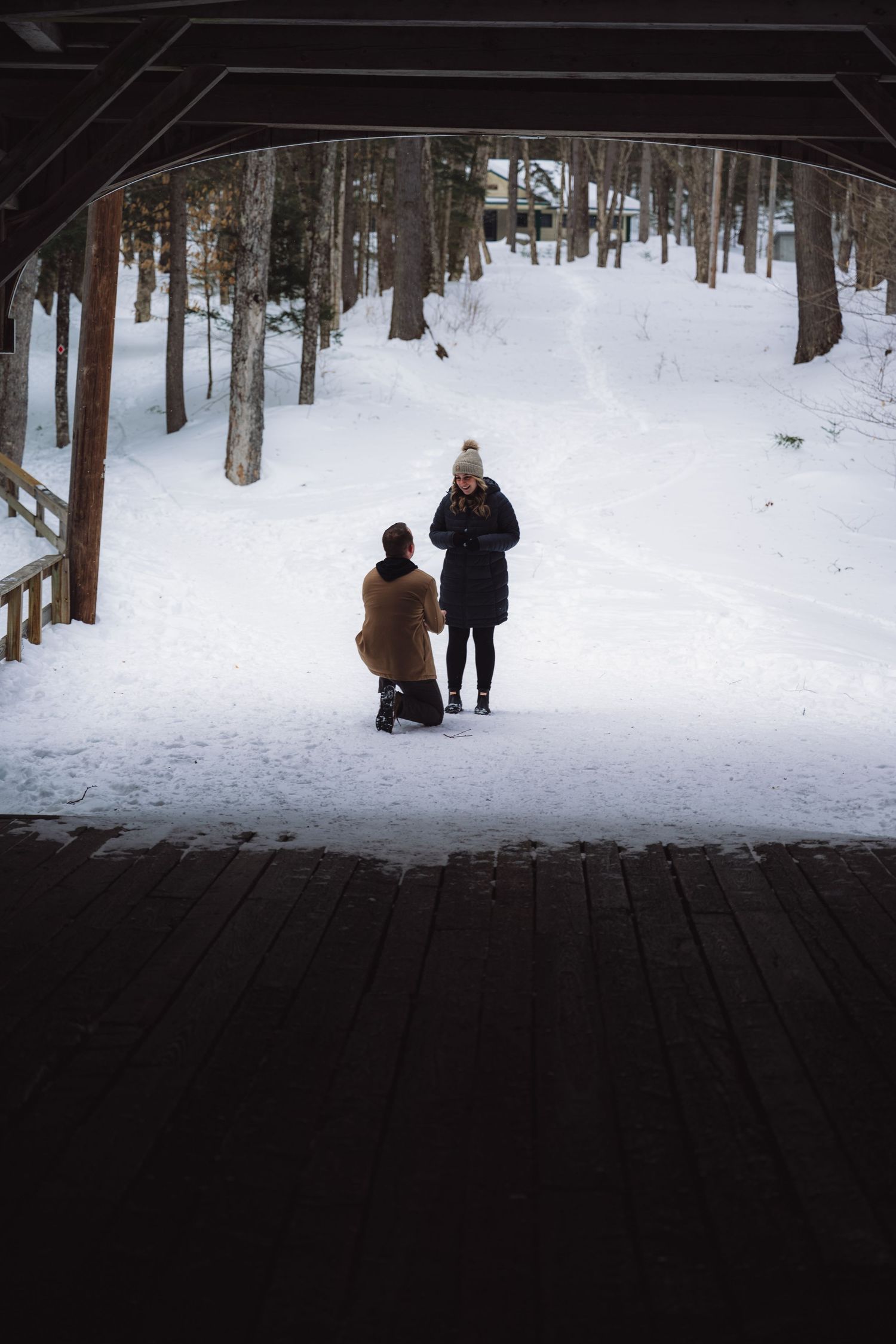 People walking through a snowy forest path during winter with tall trees creating a serene woodland scene.