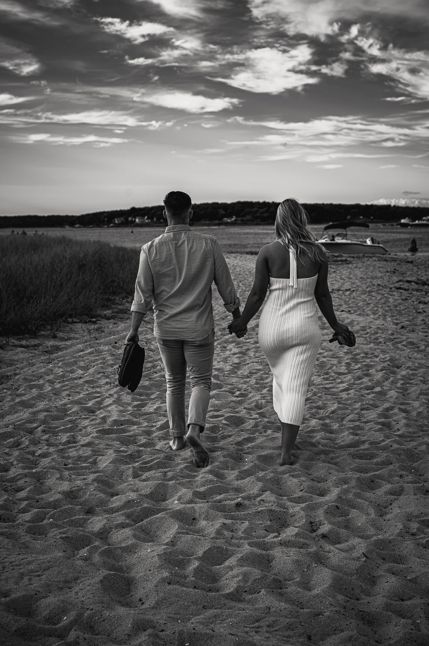 Black and white photo of people walking hand in hand on a sandy beach at sunset.