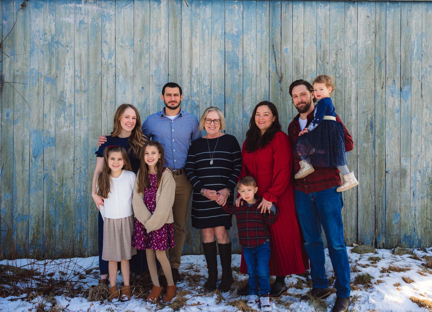 A series of family portraits taken against a rustic blue wooden fence in snowy winter conditions.