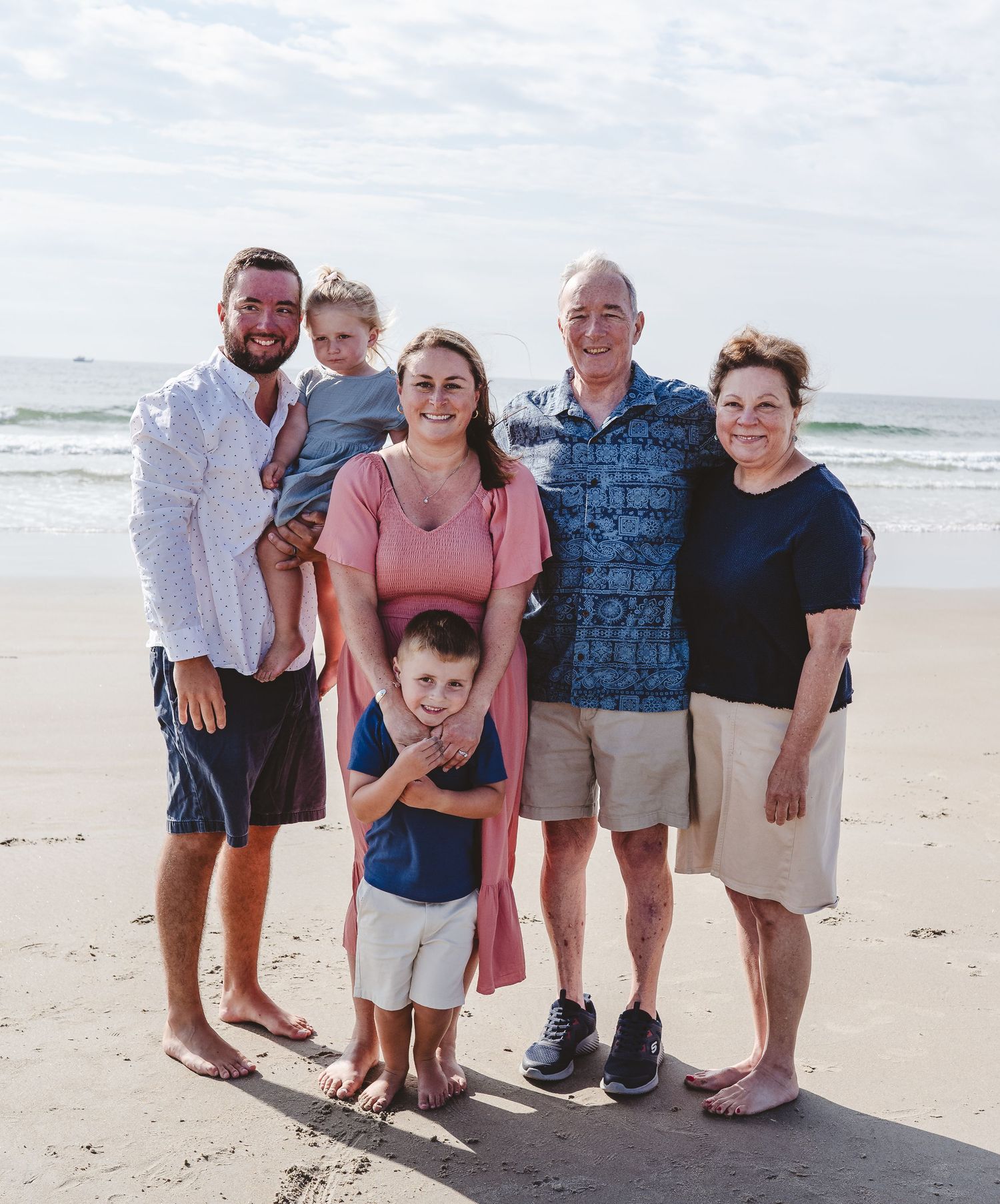 A group poses together on a sunny beach with ocean waves visible in the background.
