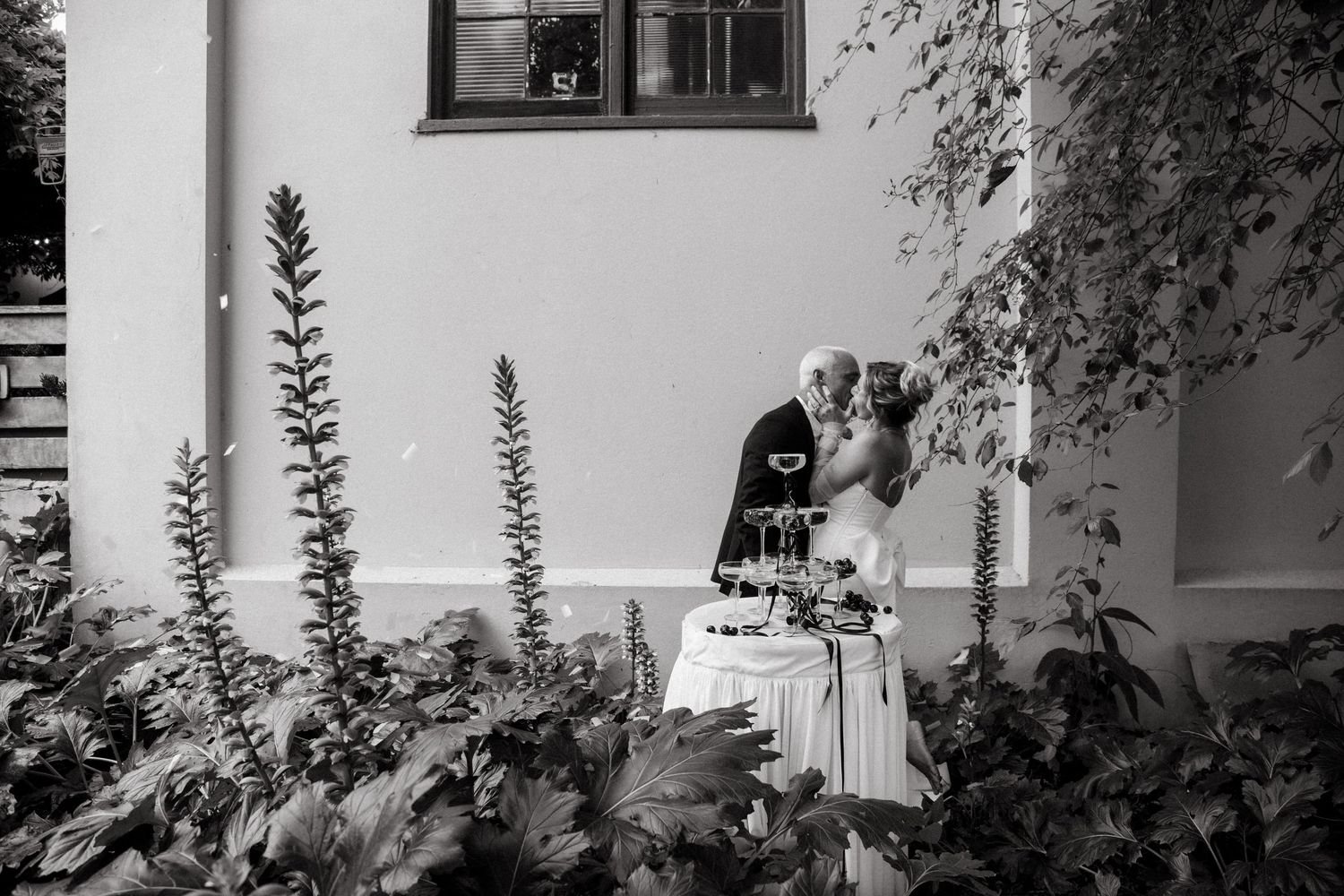 Black and white photo of a white building exterior with windows and foliage in daylight.
