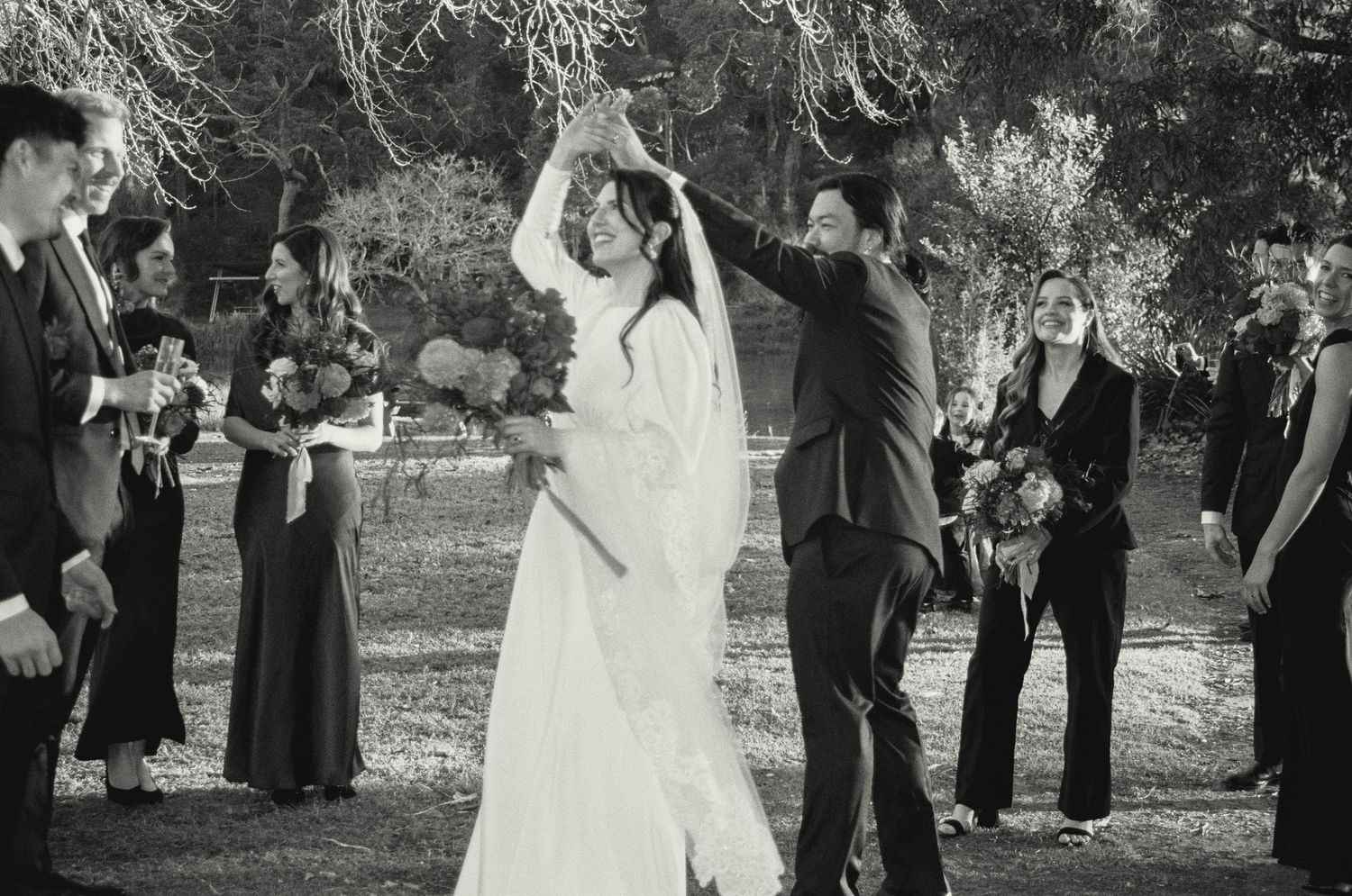 A joyful wedding celebration with people dancing outdoors in formal attire.