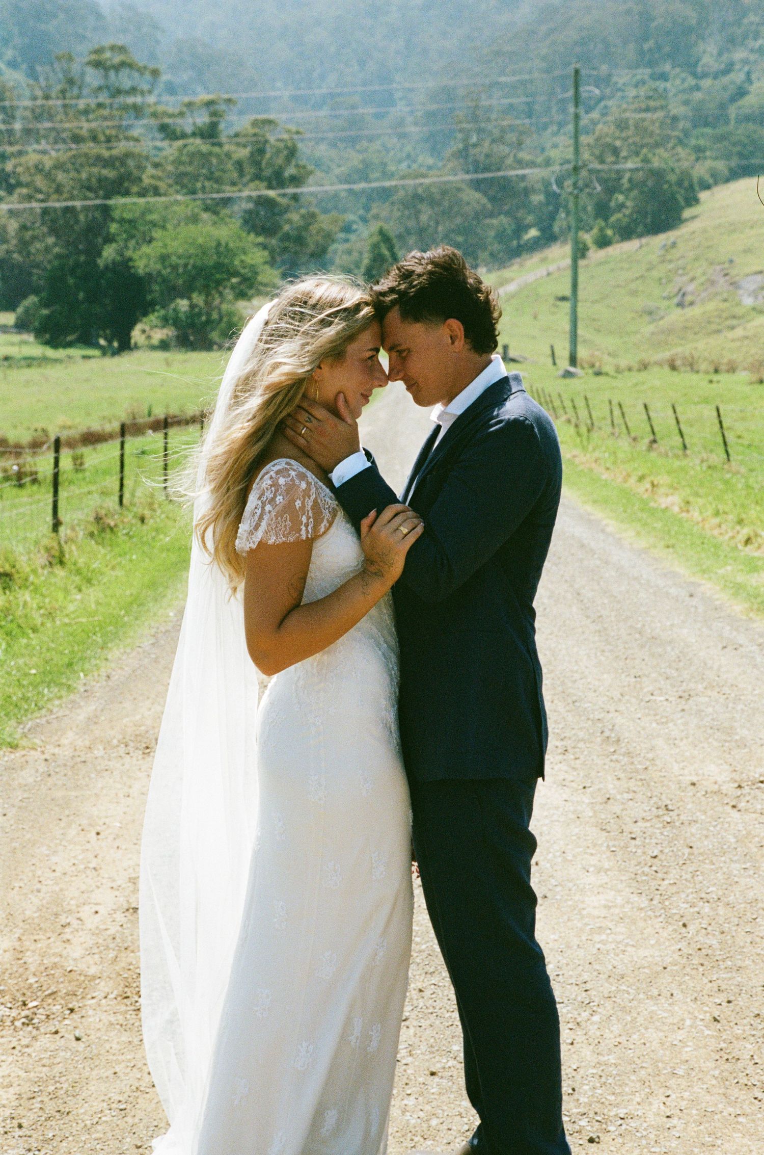Wedding couple sharing a tender moment on a country dirt road with rolling hills.