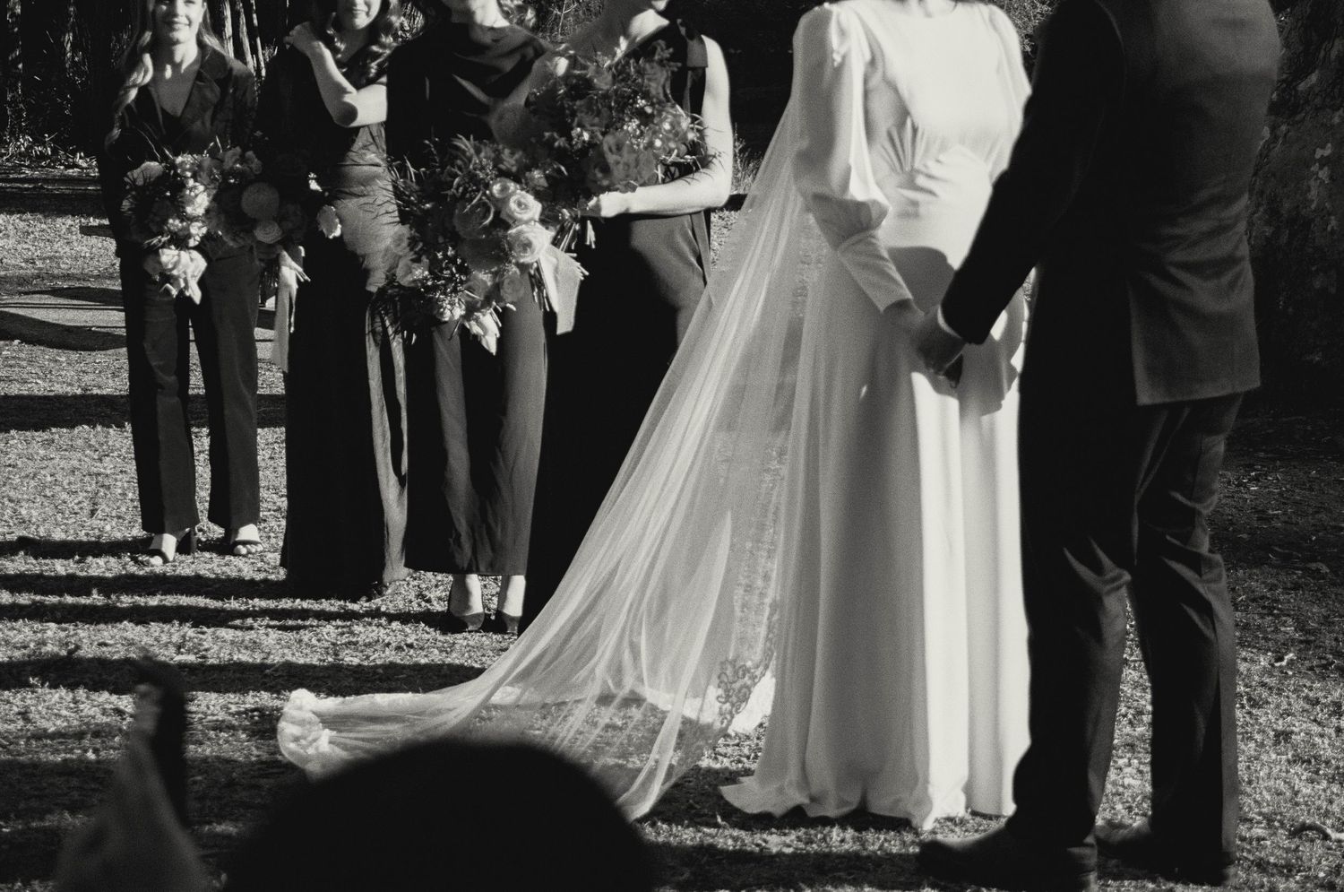 Black and white photo of a wedding ceremony with flowing white dress and veil against outdoor backdrop.