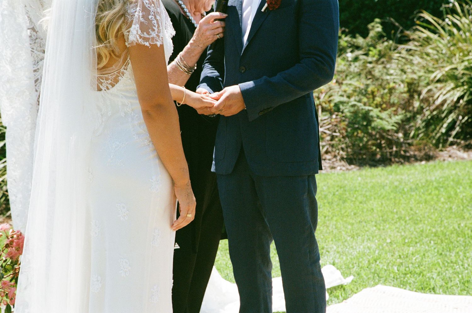 An outdoor wedding ceremony taking place on a sunny day with white columns and green grass.