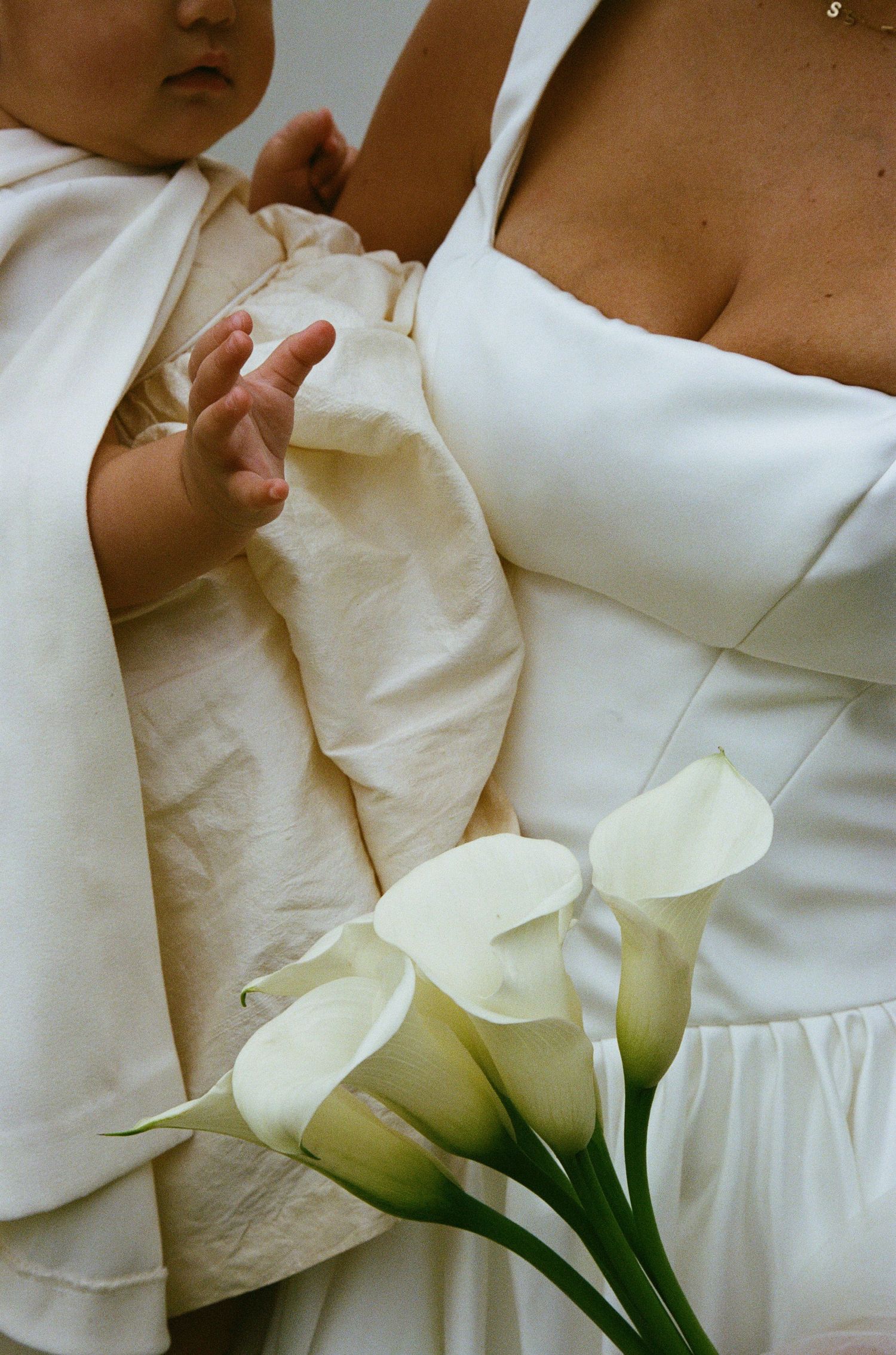 White calla lilies rest against elegant wedding attire in a close-up detail shot.