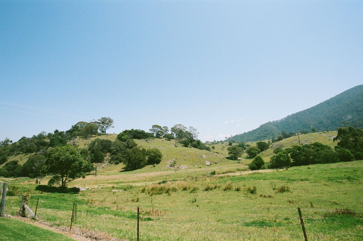 Rolling green hills and mountains stretch across a scenic pastoral landscape under blue skies.