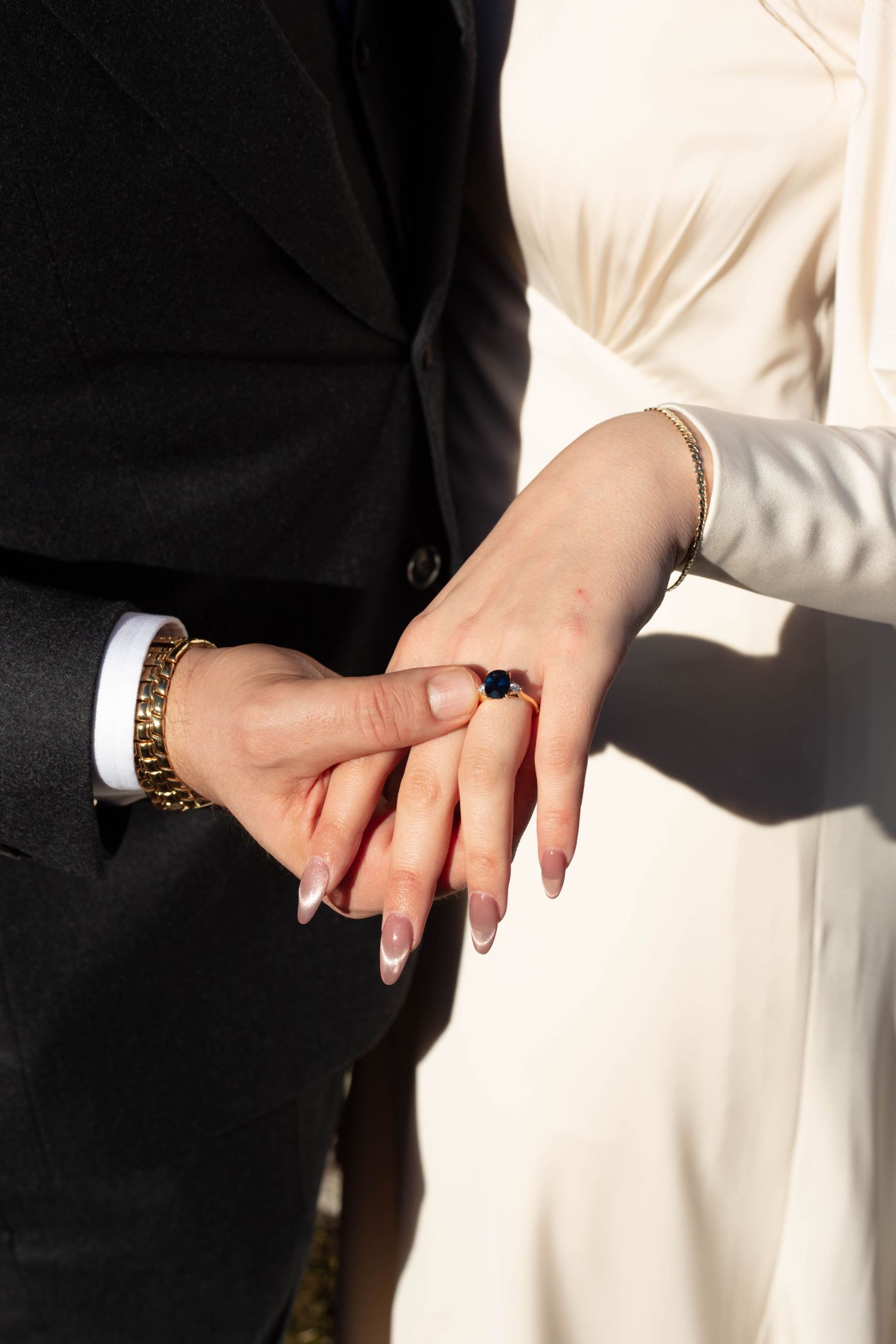 Two hands wearing wedding rings touch intimately against a black and white backdrop.