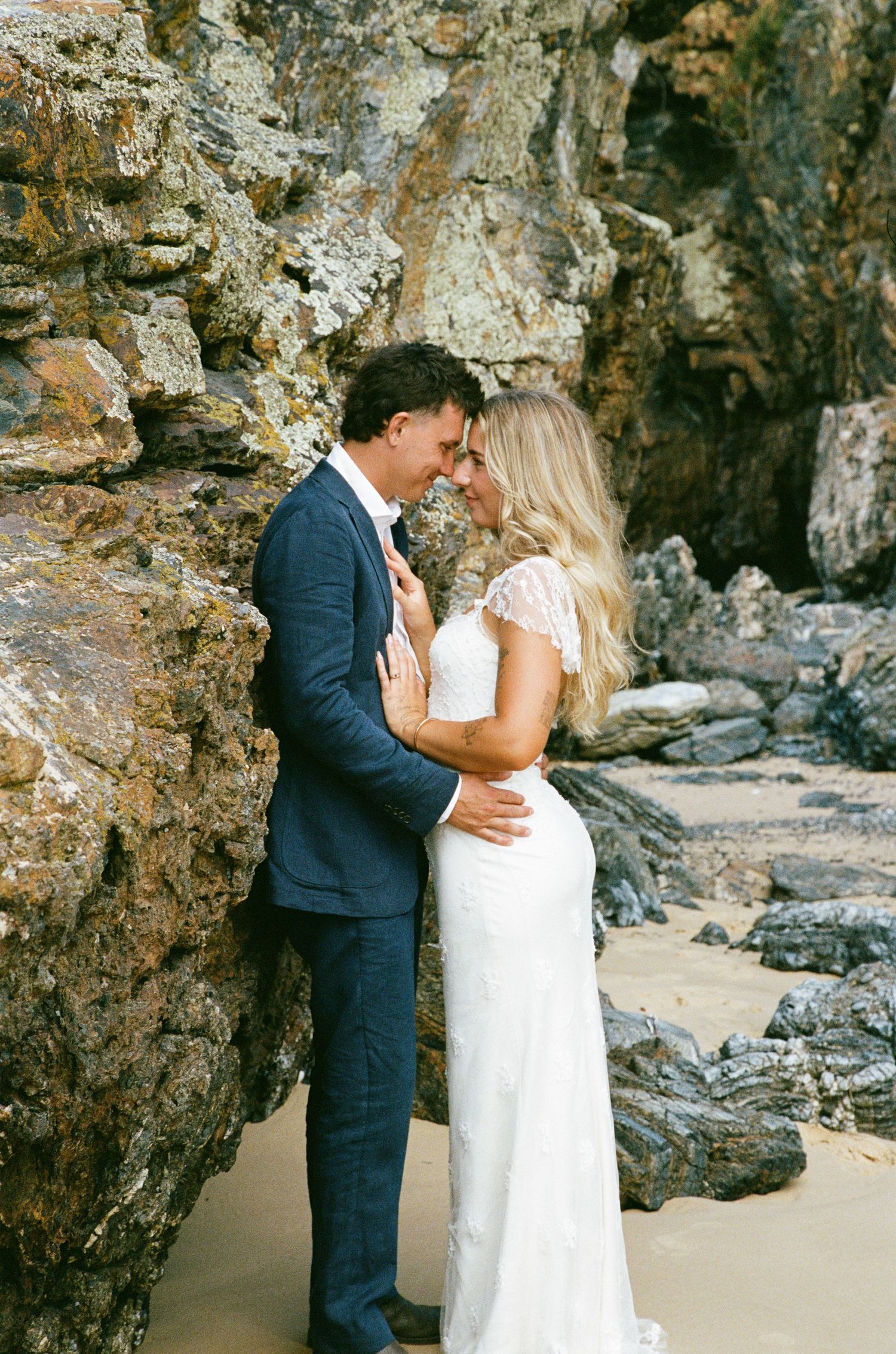 Wedding couple embracing on a rocky beach with dramatic cliffs in the background.