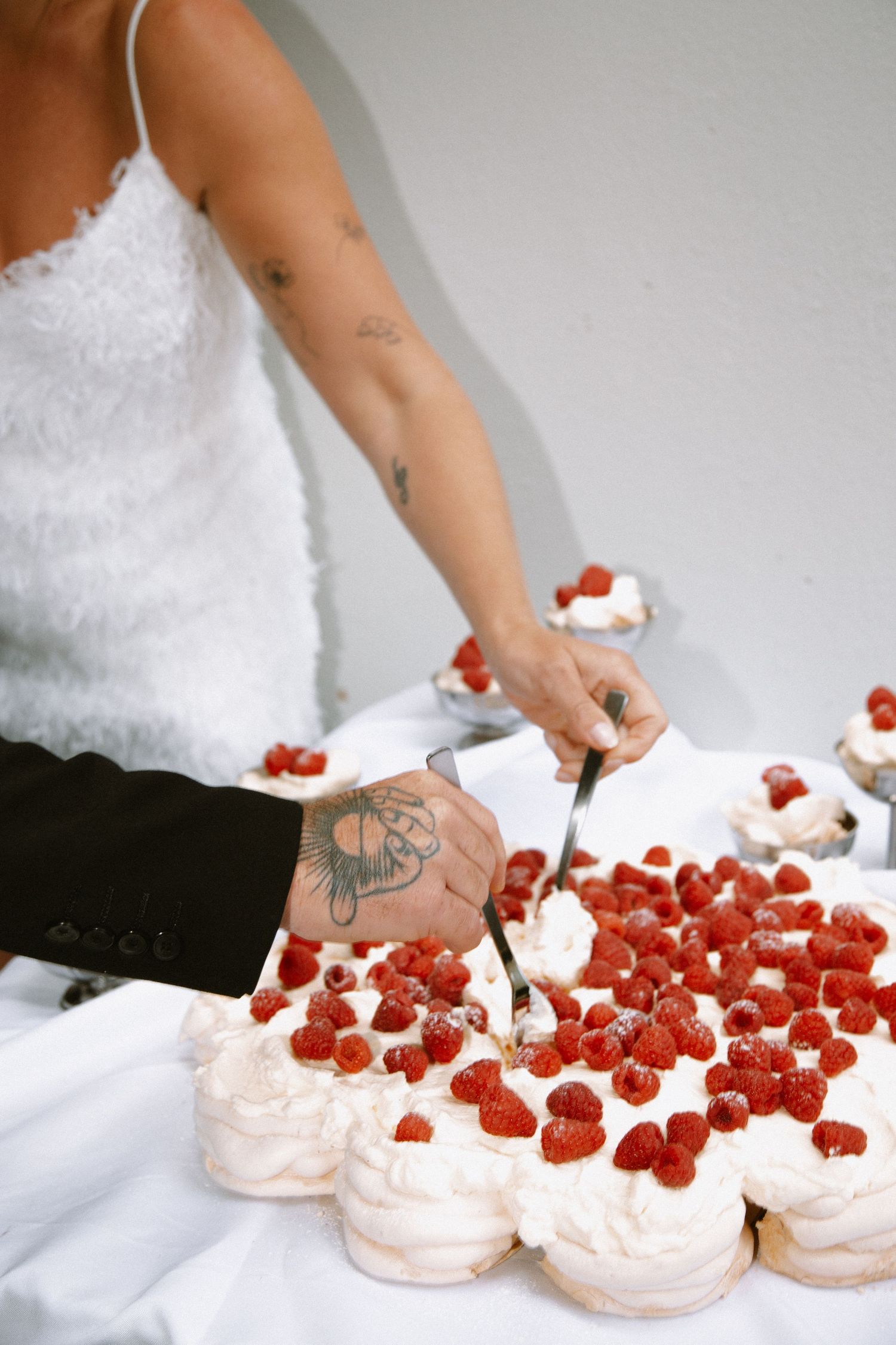 Hands arranging fresh red strawberries on white meringue desserts against a light background.