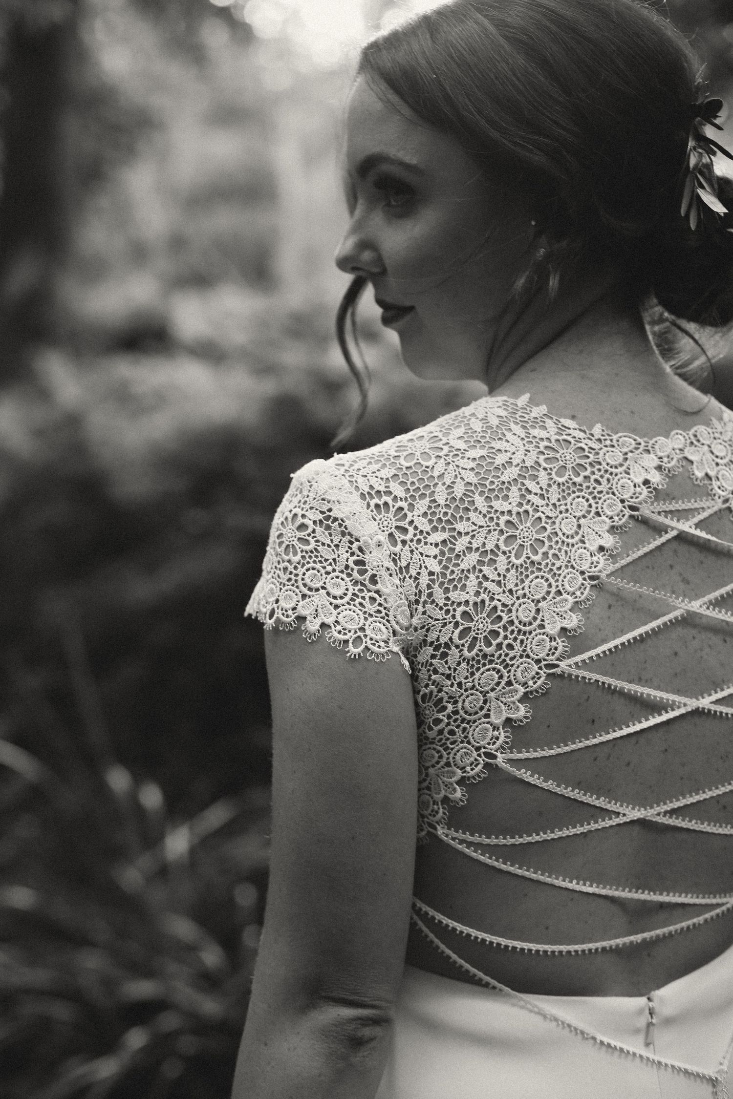 A black and white photograph of a wedding dress with delicate lace cap sleeves and pearls crisscrossing the open back.