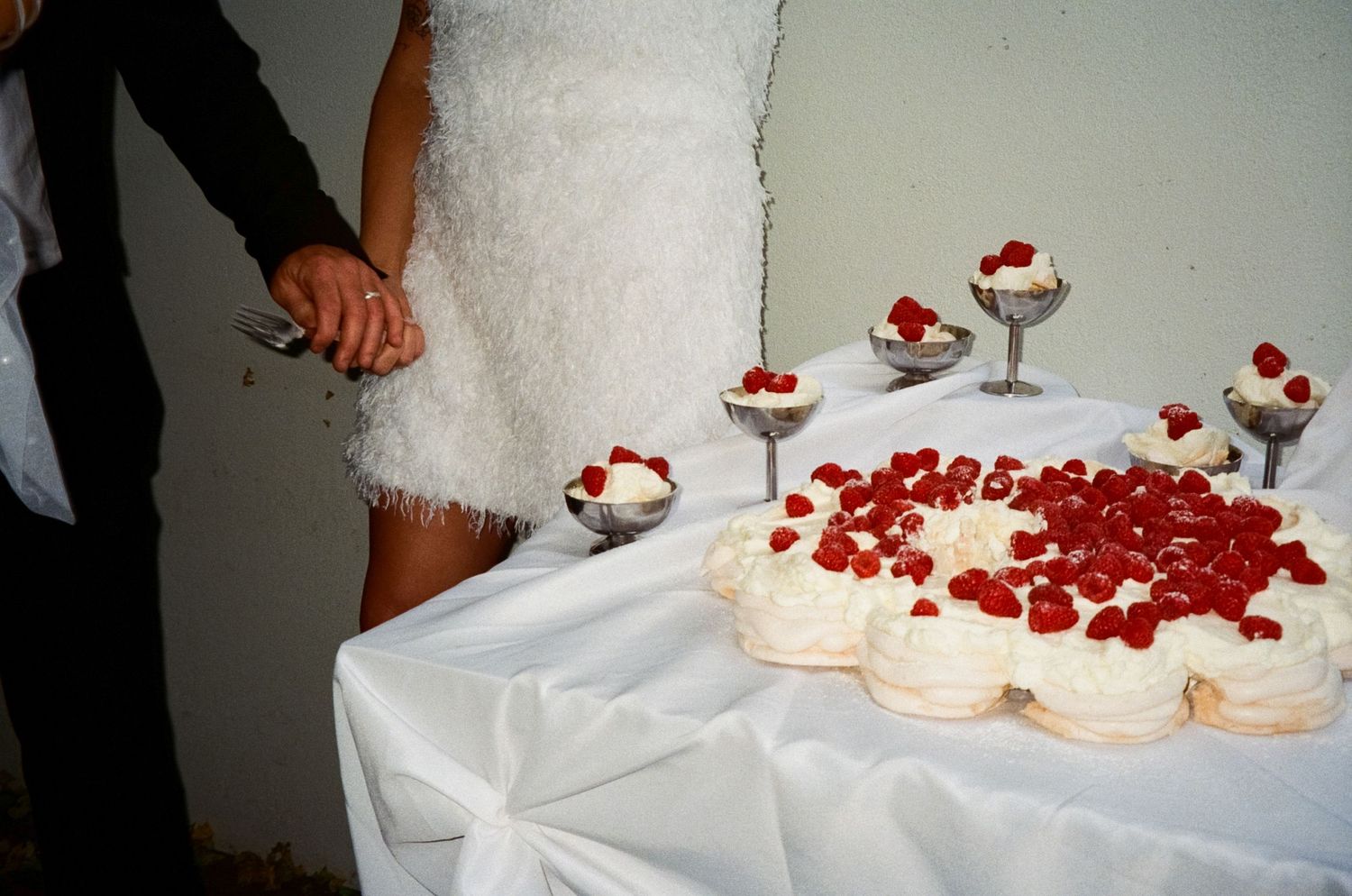 White dessert table with scattered red berries and small individual servings topped with cream and fruit.