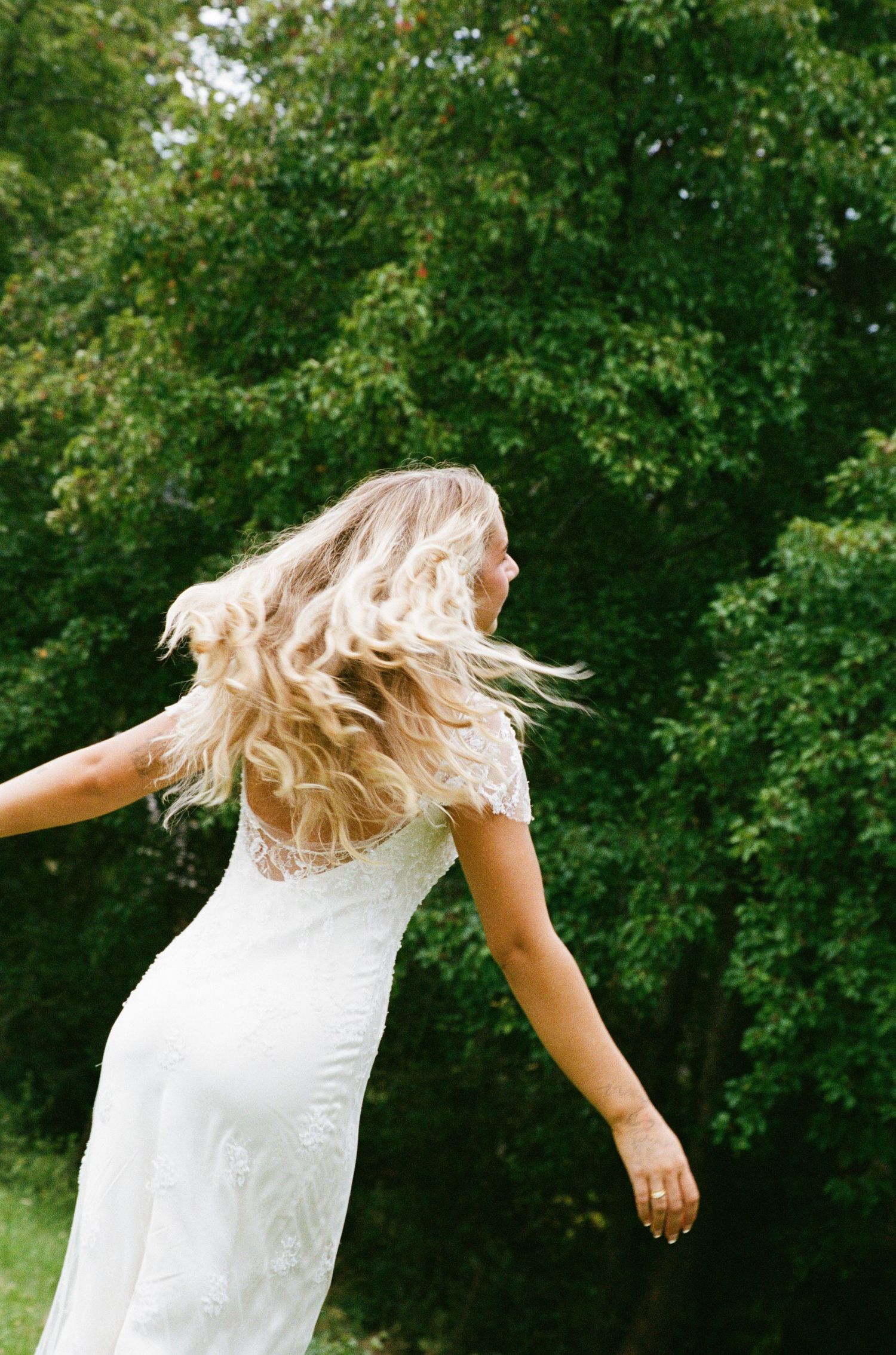 A bride in a white lace dress spins joyfully in a garden setting with her hair flowing.