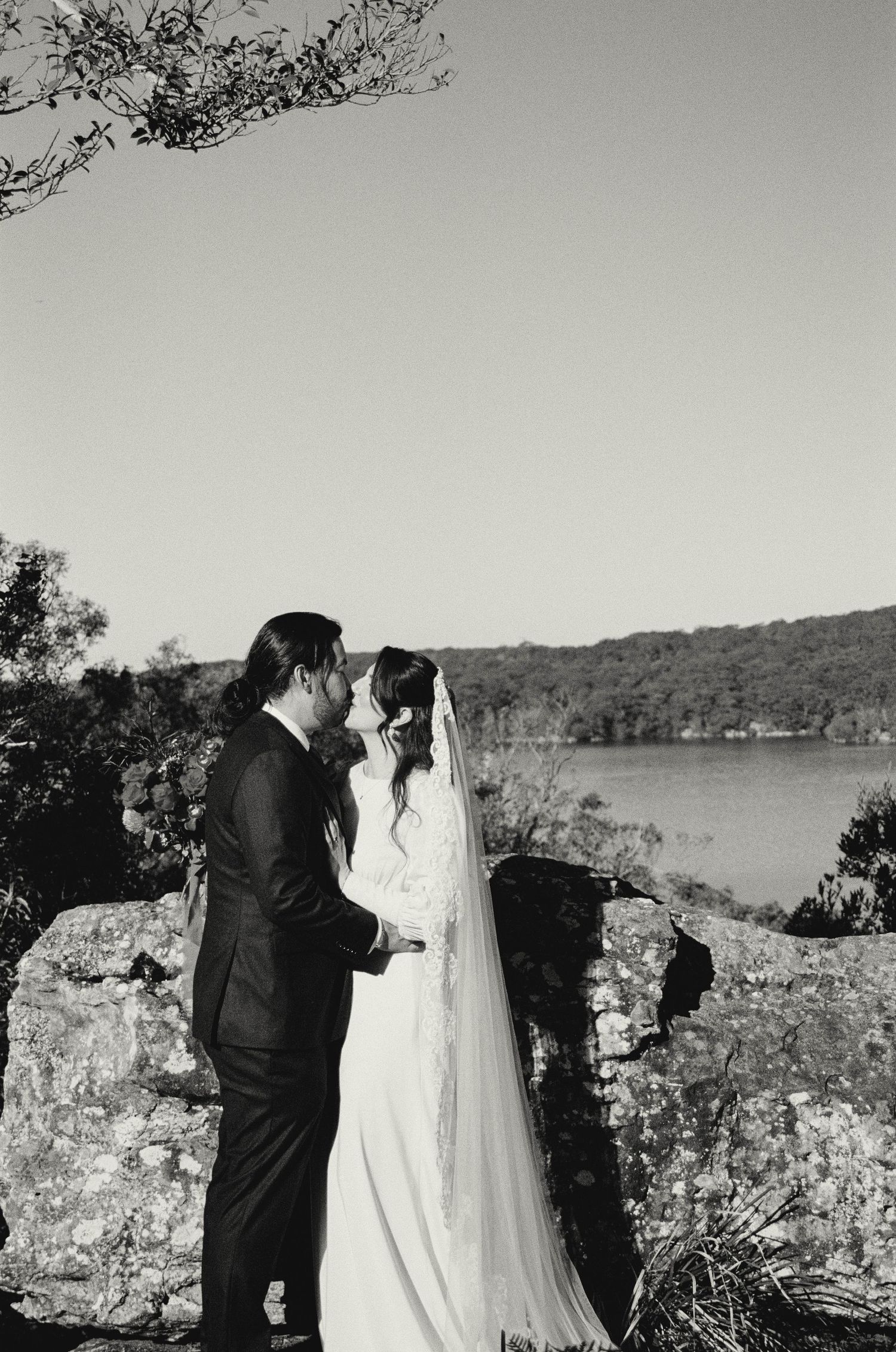 A romantic black and white wedding photo of a couple standing on rocky cliffs overlooking a serene lake.