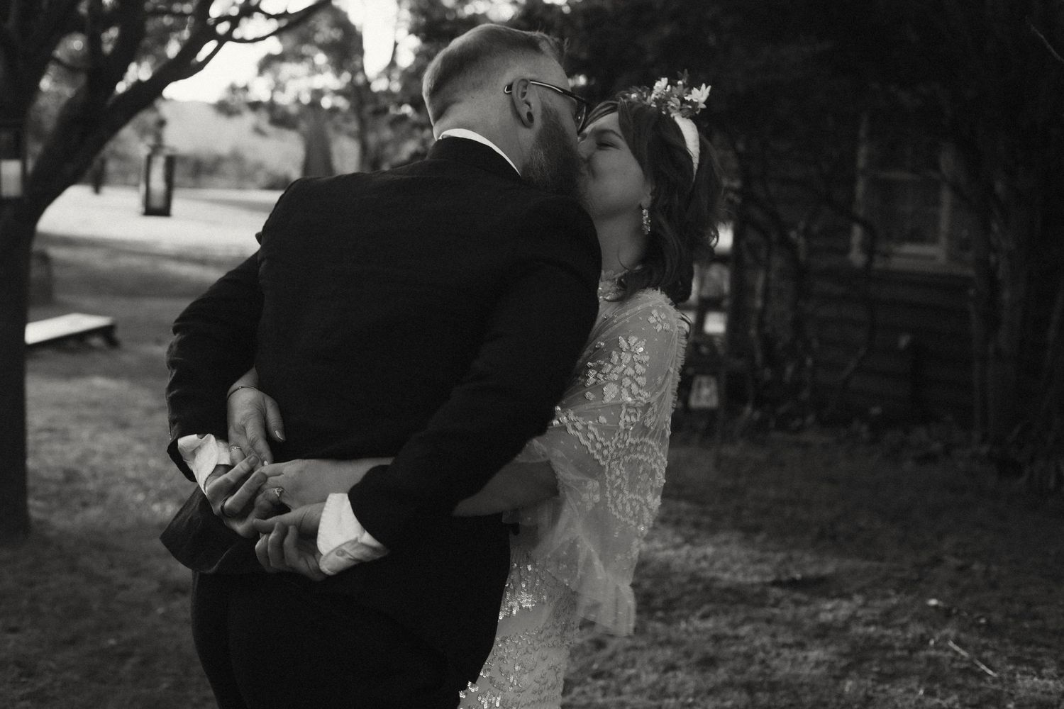 A couple performs a romantic dance move at an outdoor wedding as others watch in formal attire.