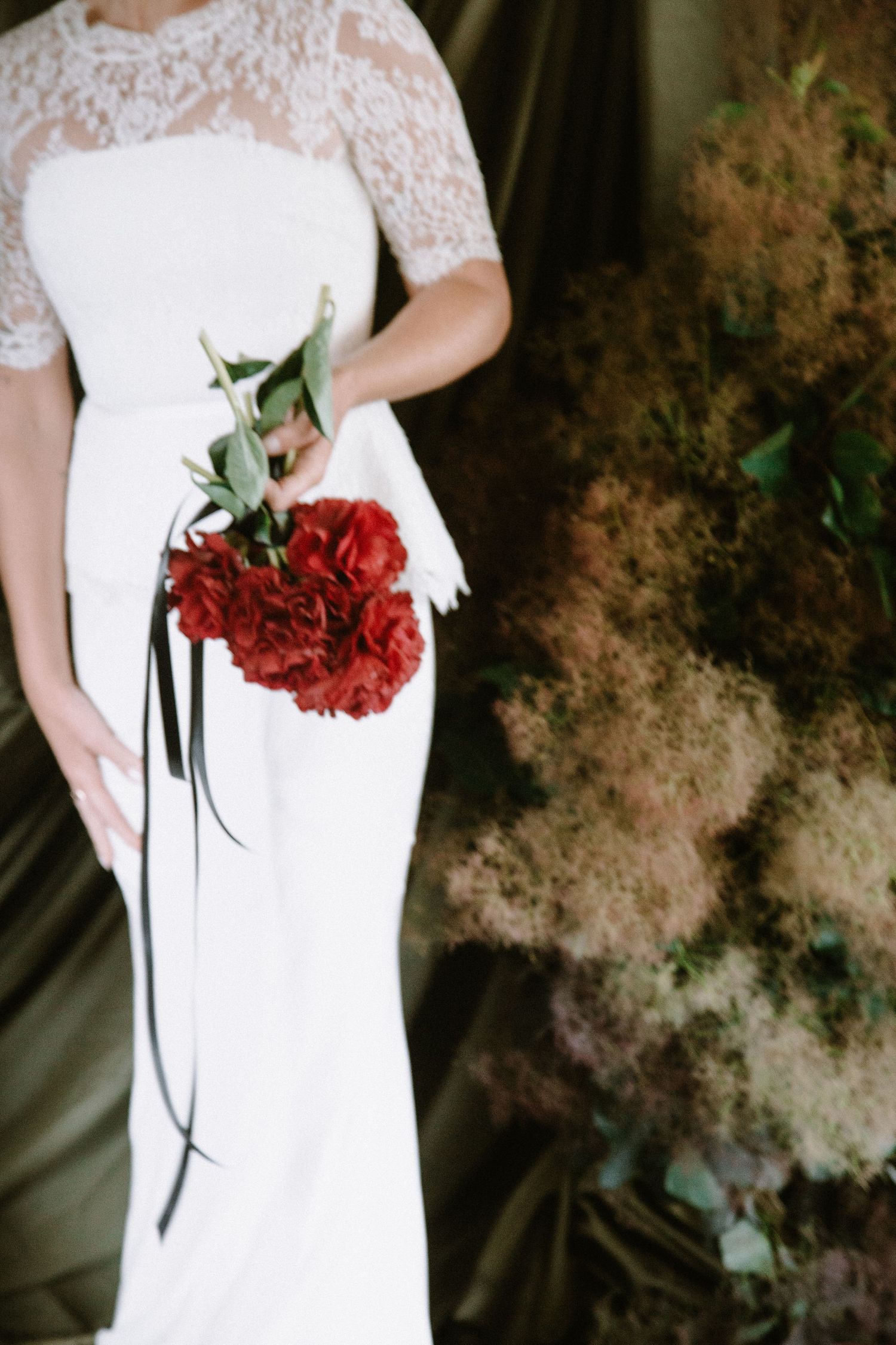 A white lace wedding dress detail with a red rose bouquet held against it.