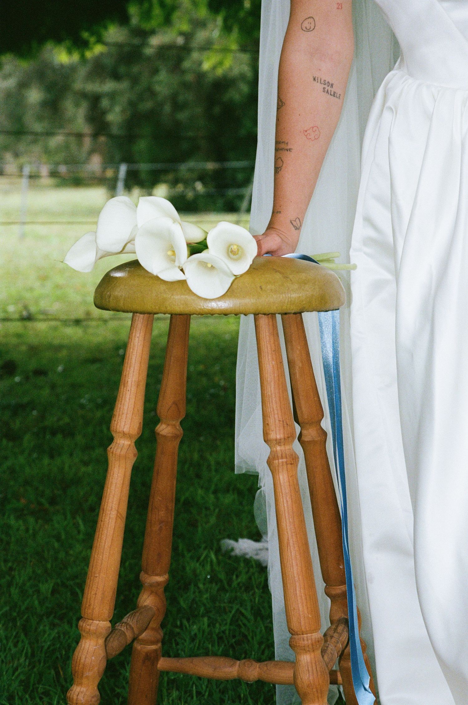 White calla lilies rest elegantly on a wooden stool against a green outdoor background.