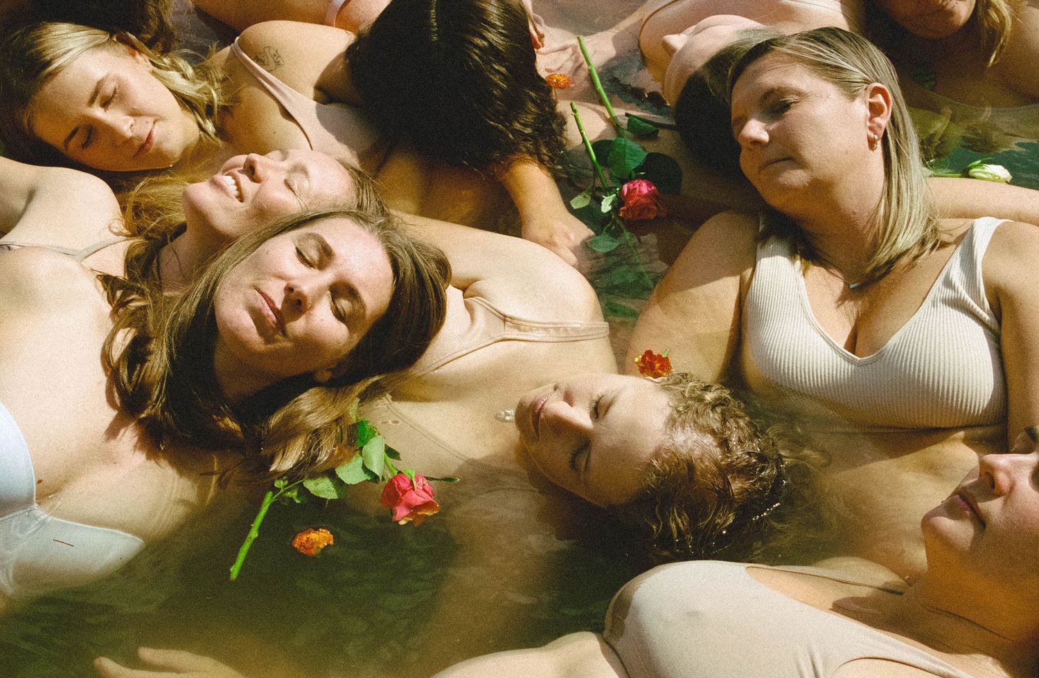 A group of people lying down together with flowers scattered around them in an artistic composition.