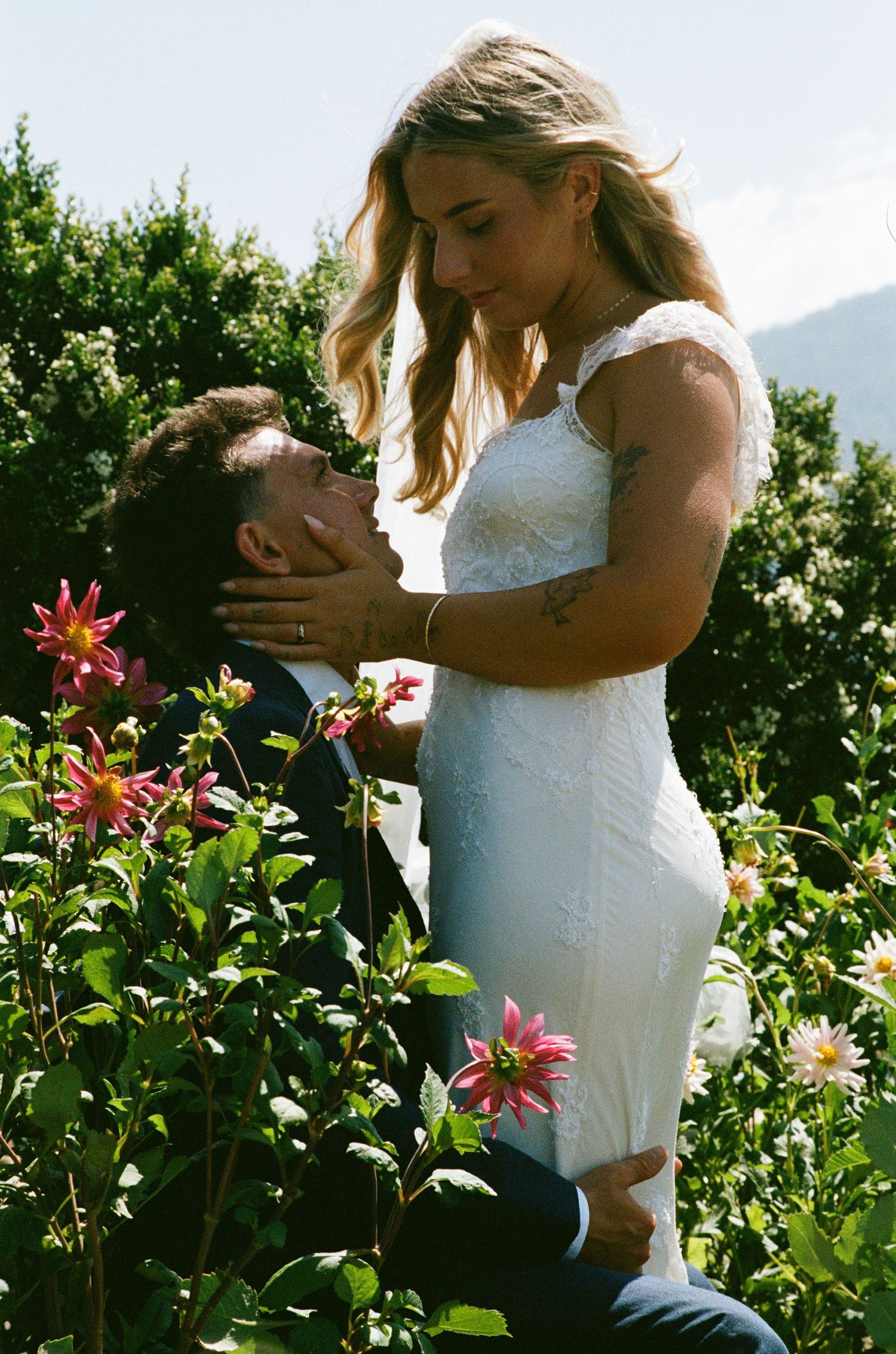 Newlyweds share an intimate moment among blooming dahlias in a garden.