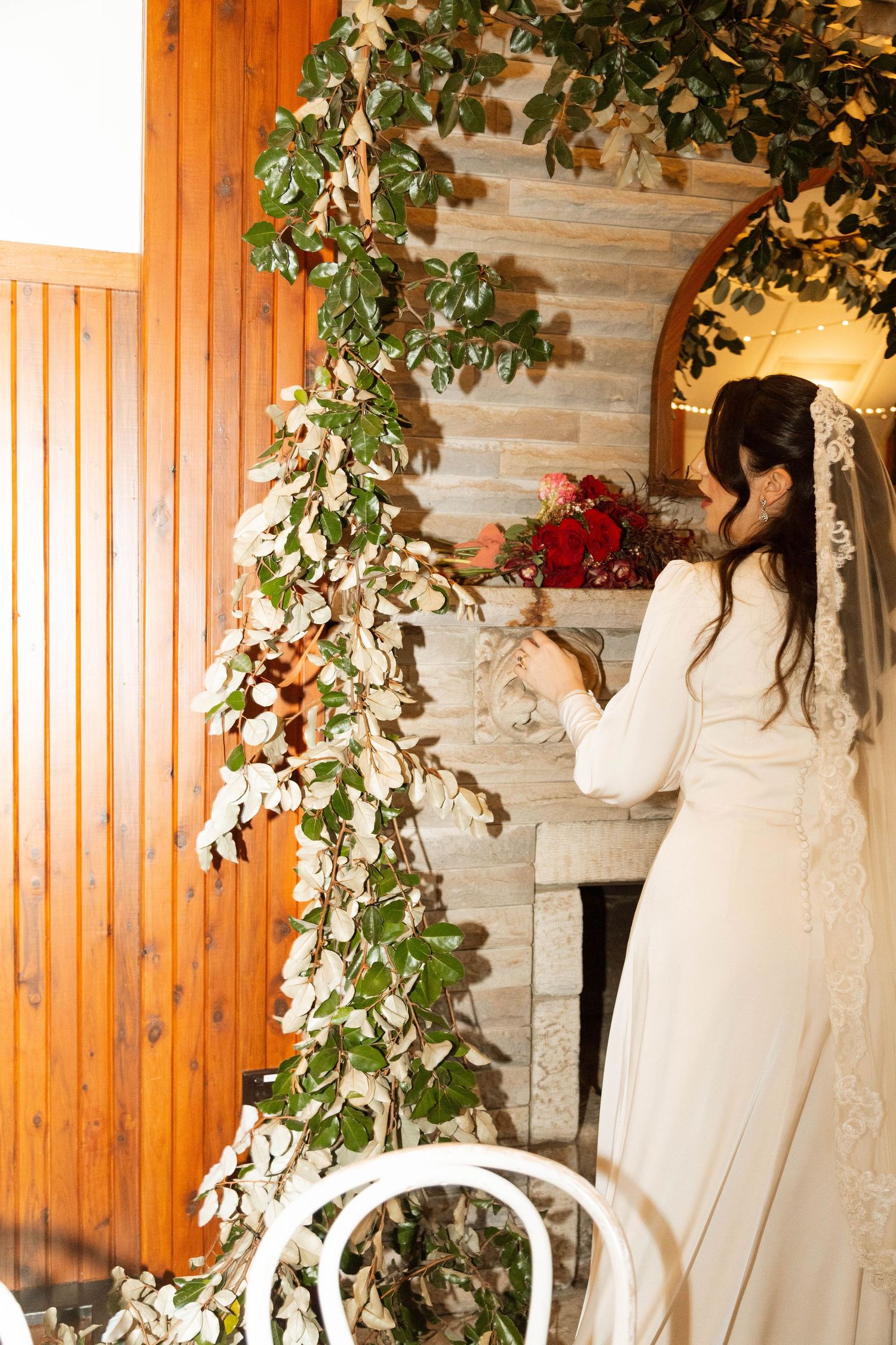 Wedding gowns displayed against wooden paneled walls adorned with cascading greenery and white floral arrangements.