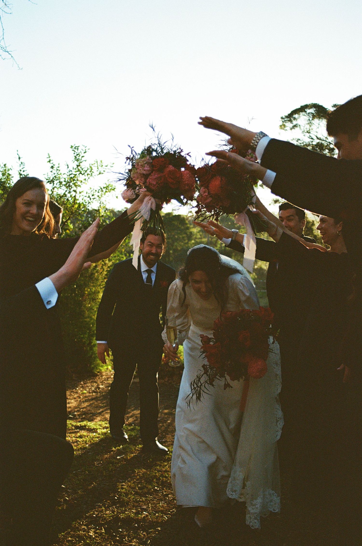 Wedding party celebrating outdoors with raised arms against a blue sky.