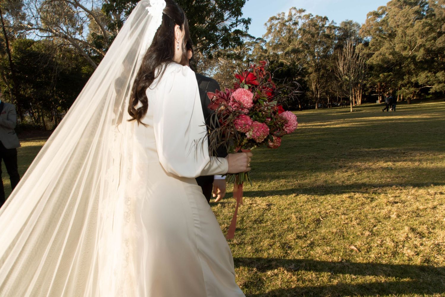 A flowing white wedding dress and veil captured against a sunlit garden with blooming bougainvillea.