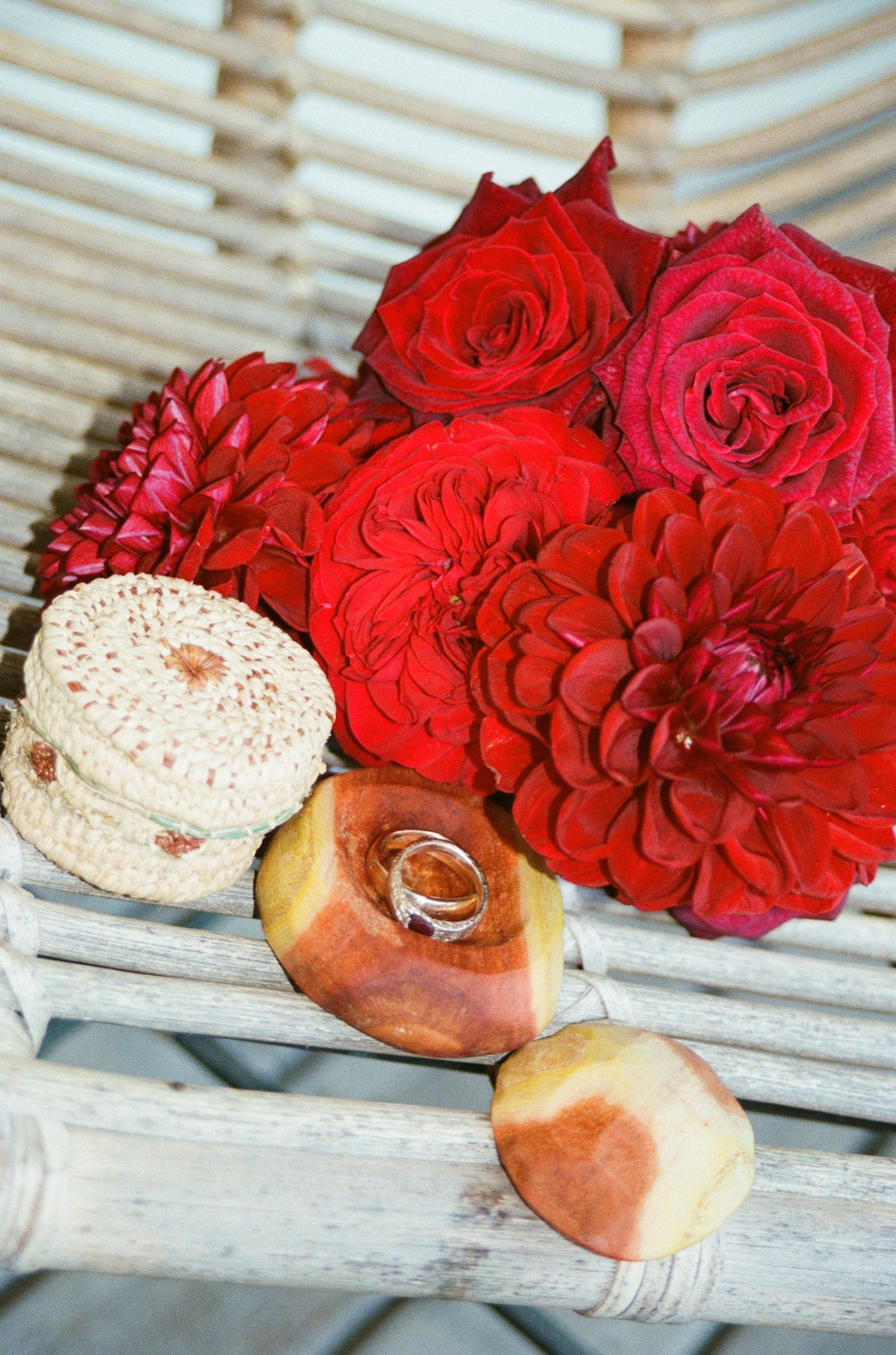 Wedding rings rest on a rustic wooden bench alongside vibrant red roses and fresh baked bread.