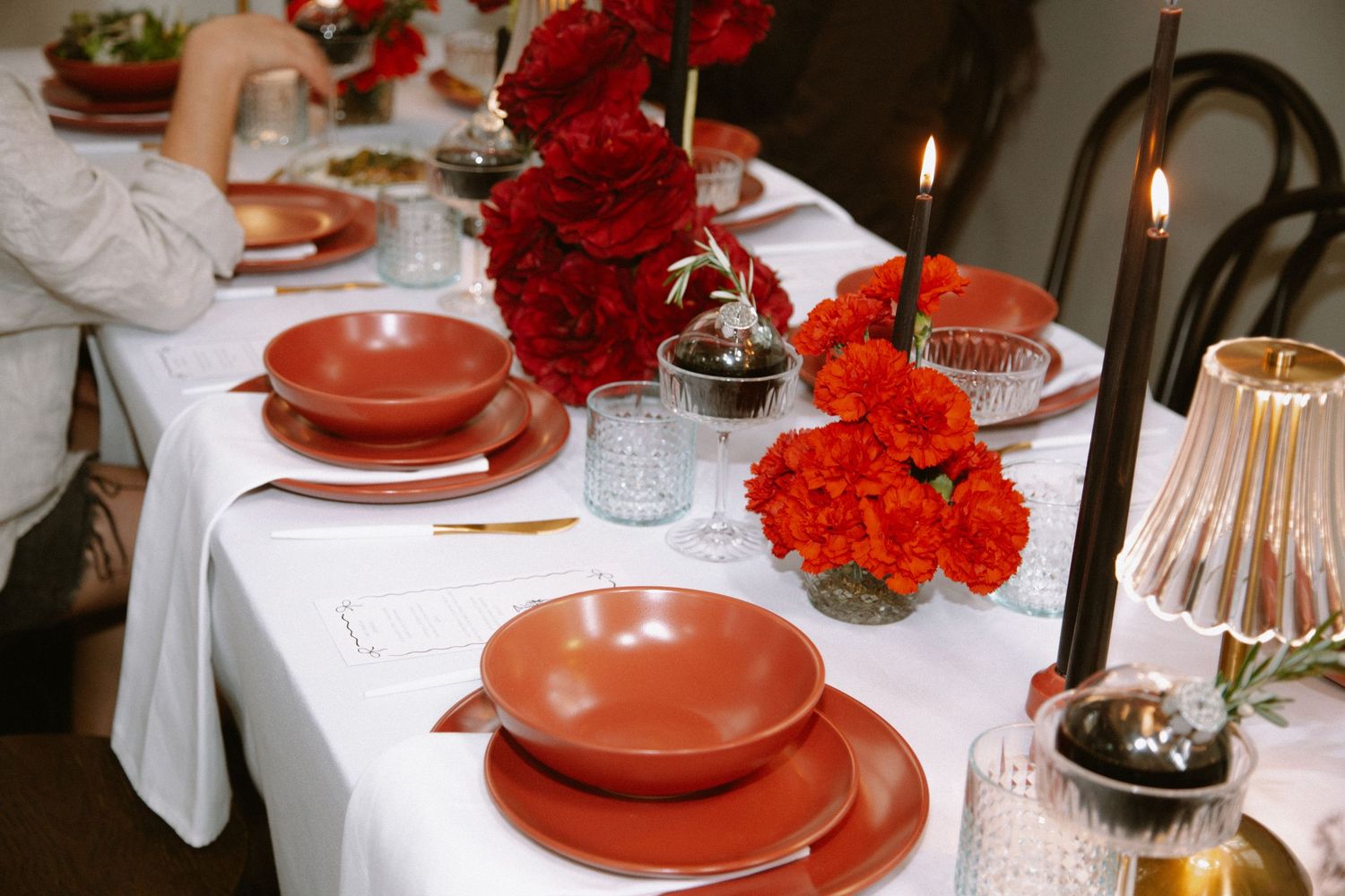 An elegant table setting with red roses and terracotta plates on white linens.