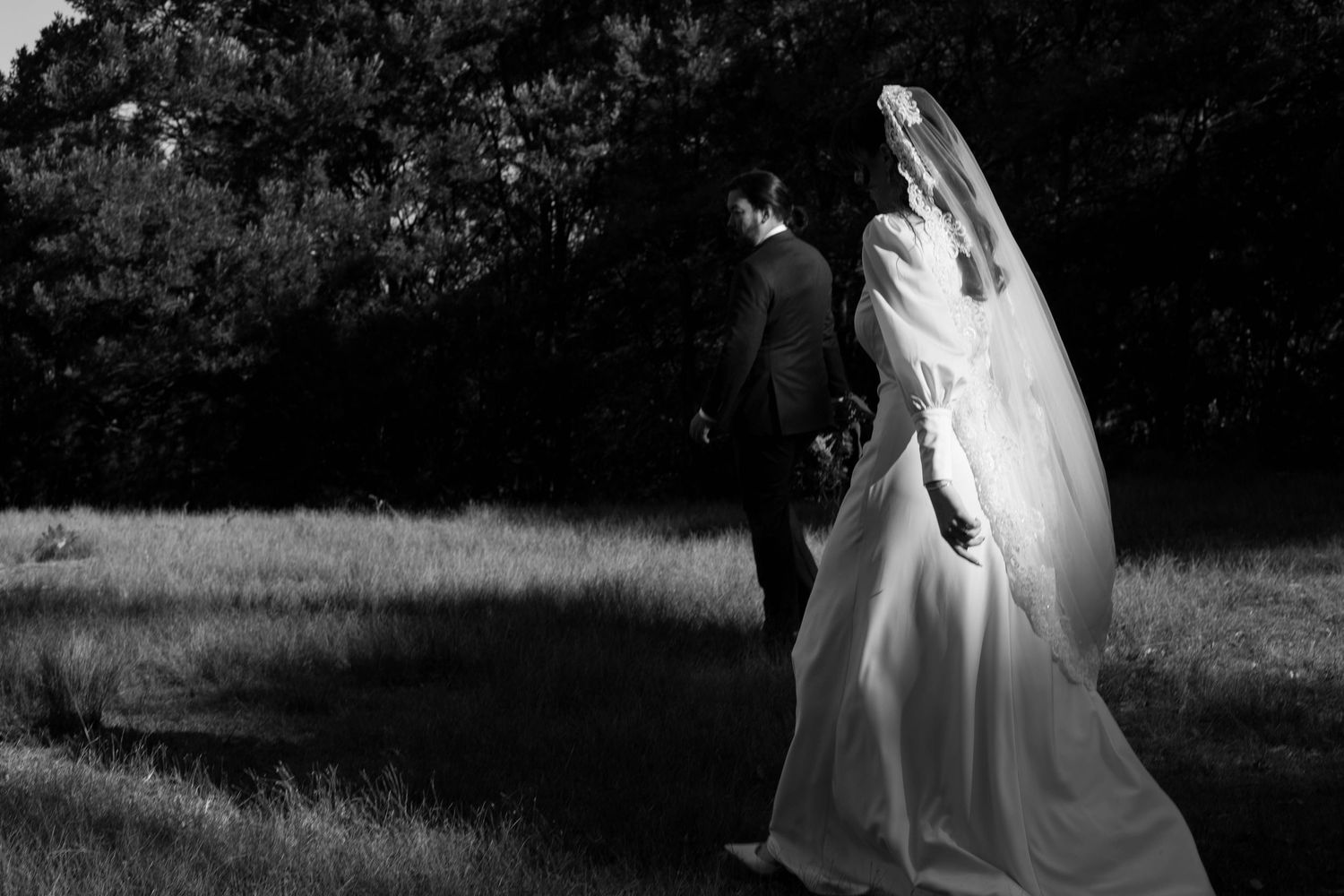 A dramatic black and white silhouette of newlyweds walking through a meadow.