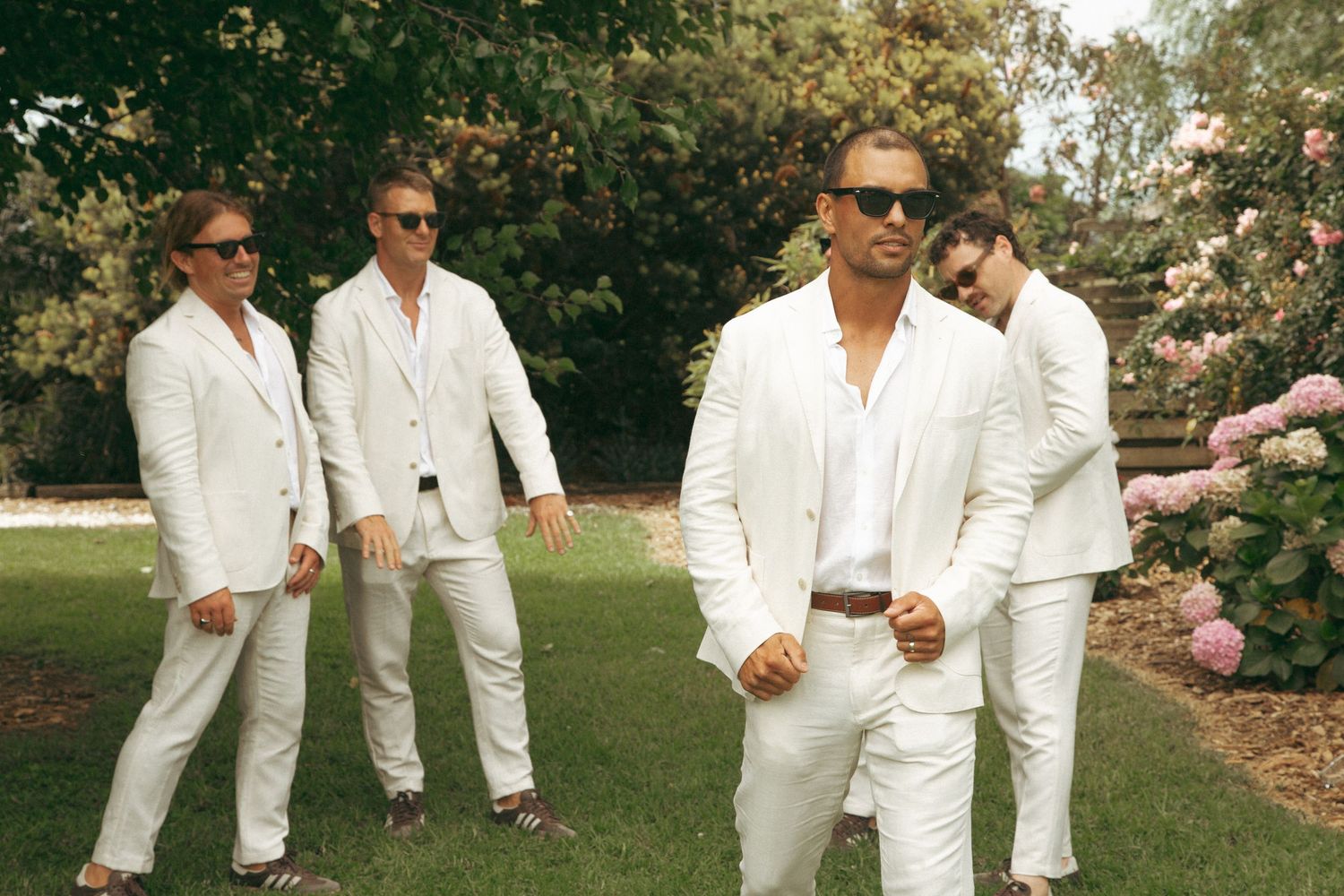 Group in white attire relaxing together on a grassy lawn during a sunny summer day.