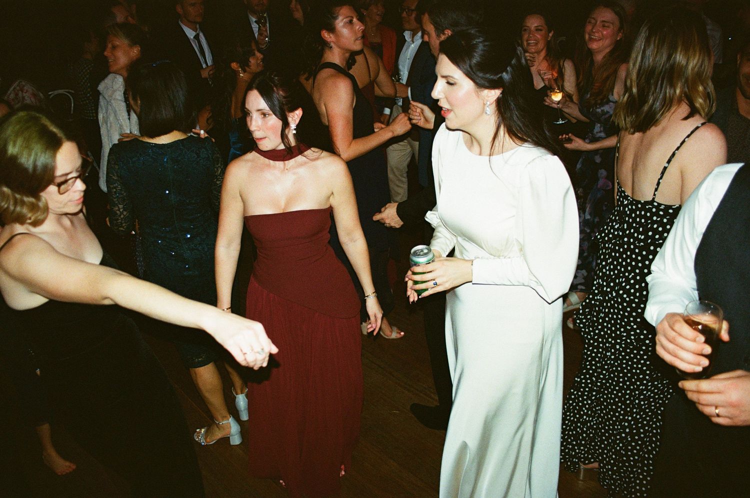 People dance and celebrate at a party wearing formal dresses in burgundy, white and black.