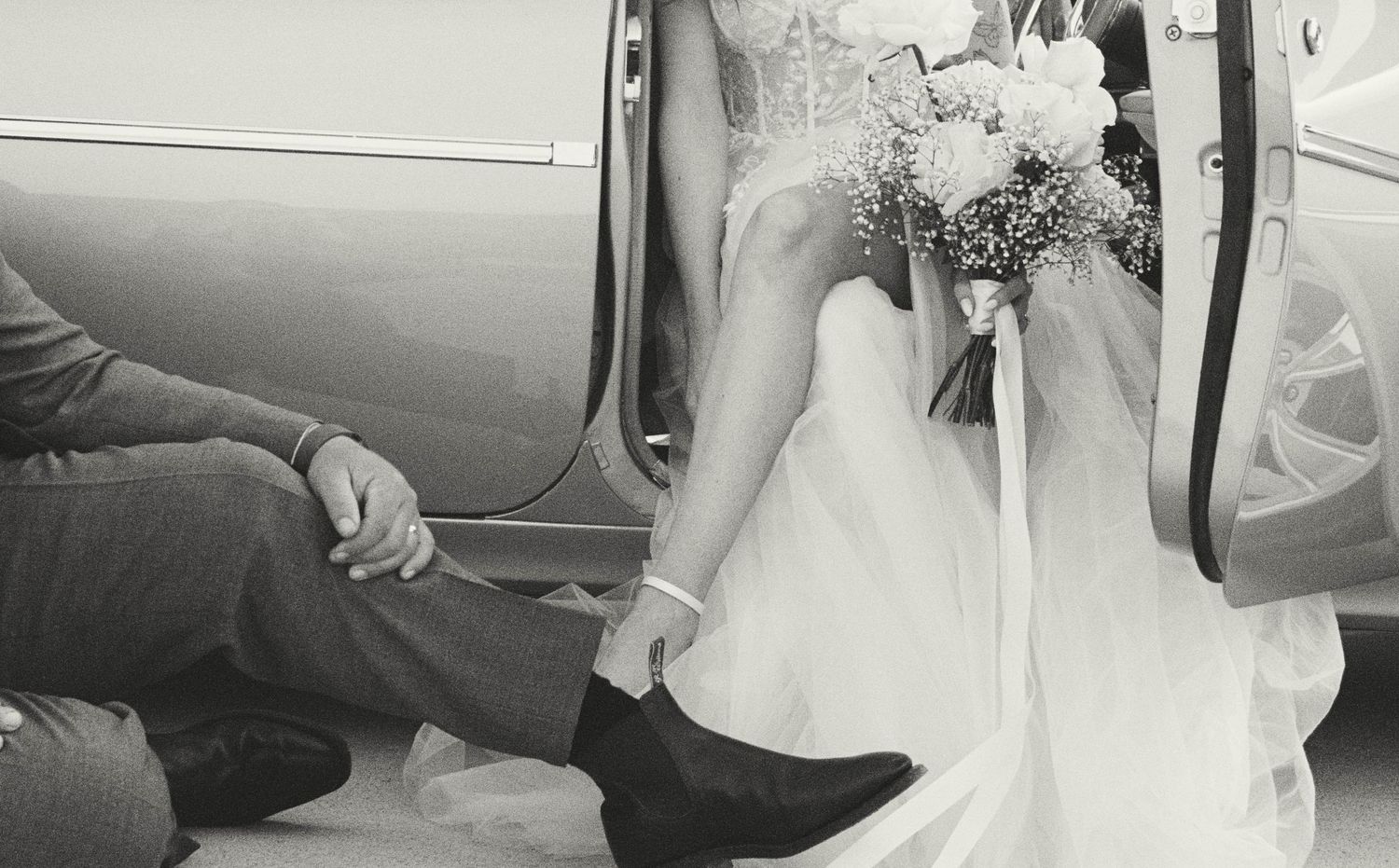 A bride in a flowing white wedding dress and veil steps into a classic car on her special day.