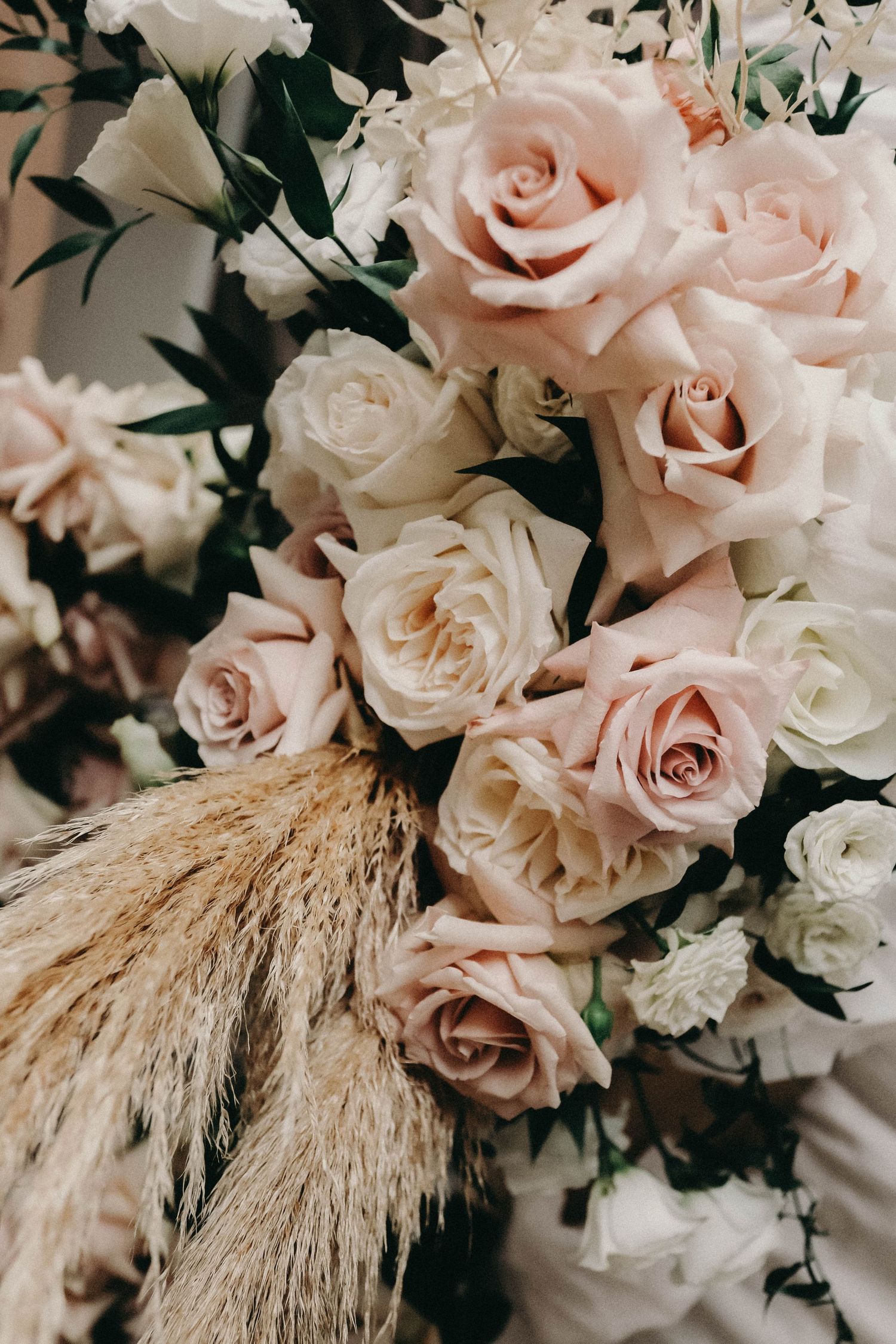 Elegant blush pink roses arranged with dried pampas grass creating a romantic wedding bouquet aesthetic.