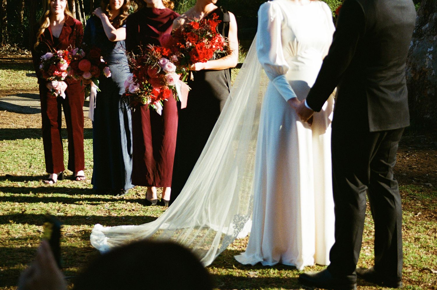 Elegant white wedding dress with flowing train shown during an outdoor autumn ceremony with bridesmaids in burgundy.