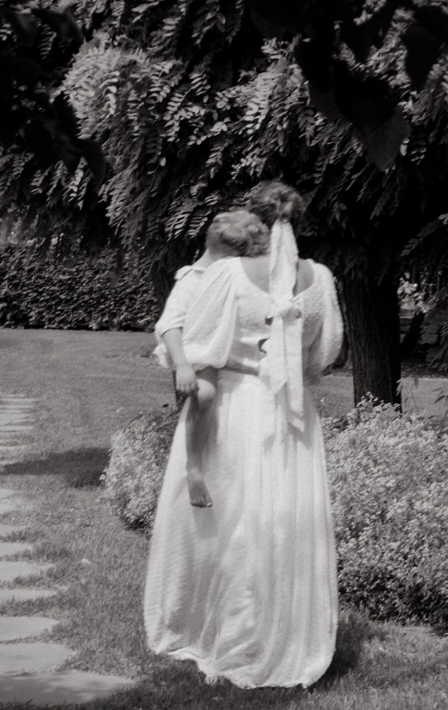 Black and white photo of a bride in a flowing dress walking in a garden setting.