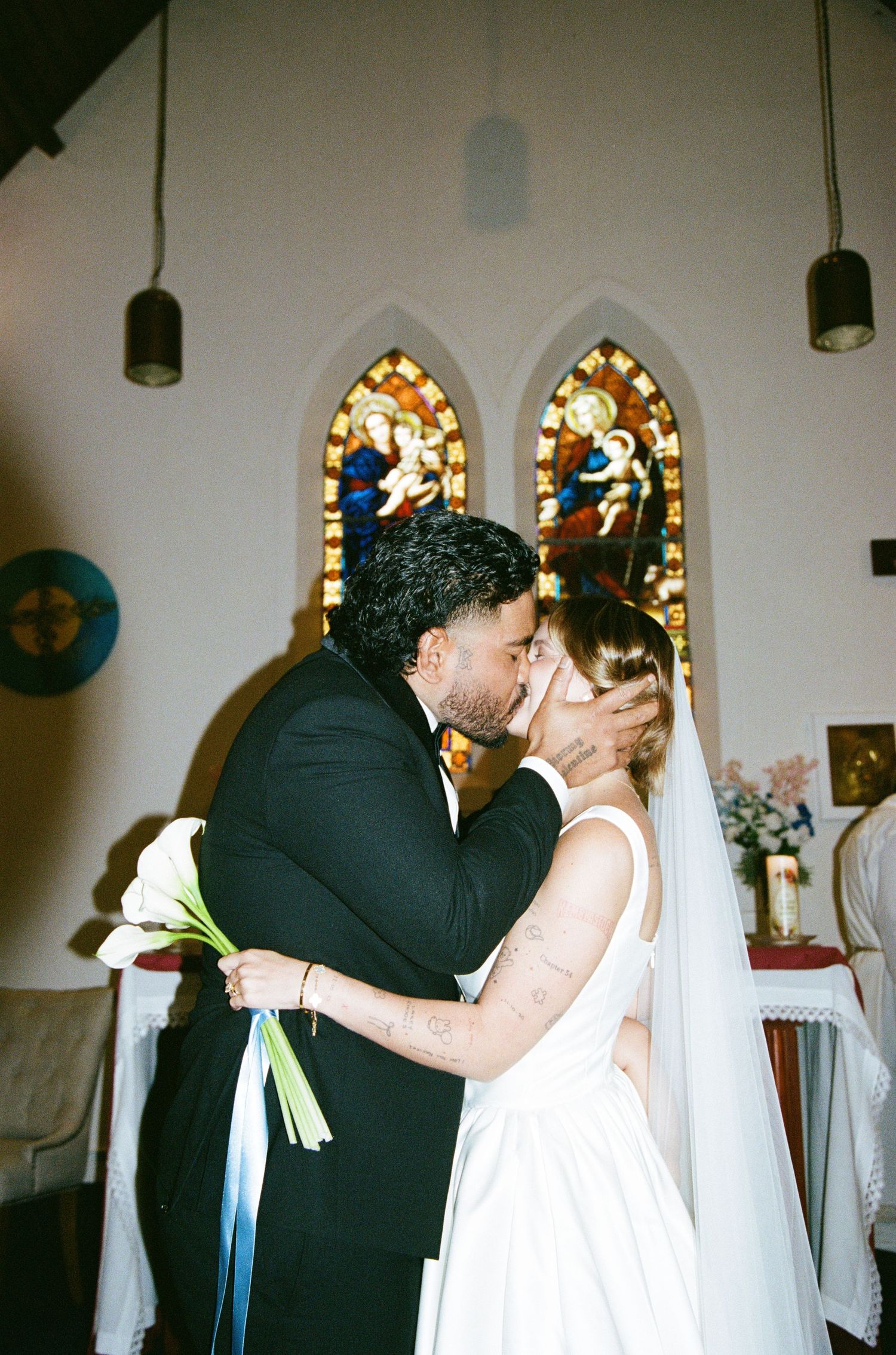 A couple shares their first kiss as newlyweds in a church with stained glass windows.