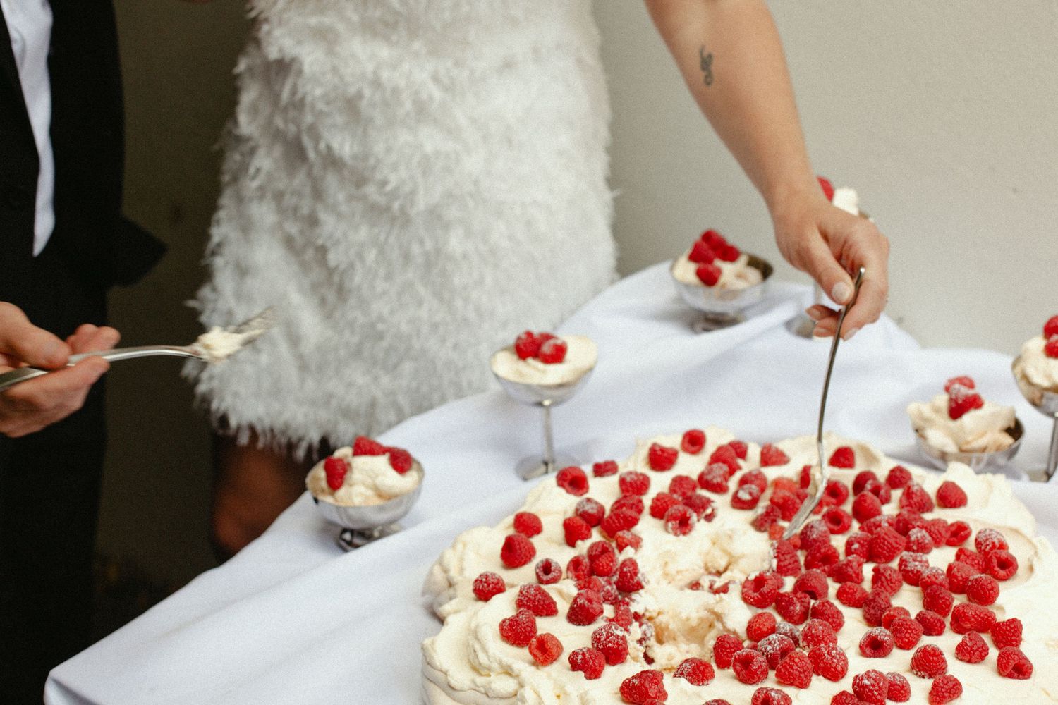 Hands decorating a white wedding cake with fresh red raspberries and cream piping.