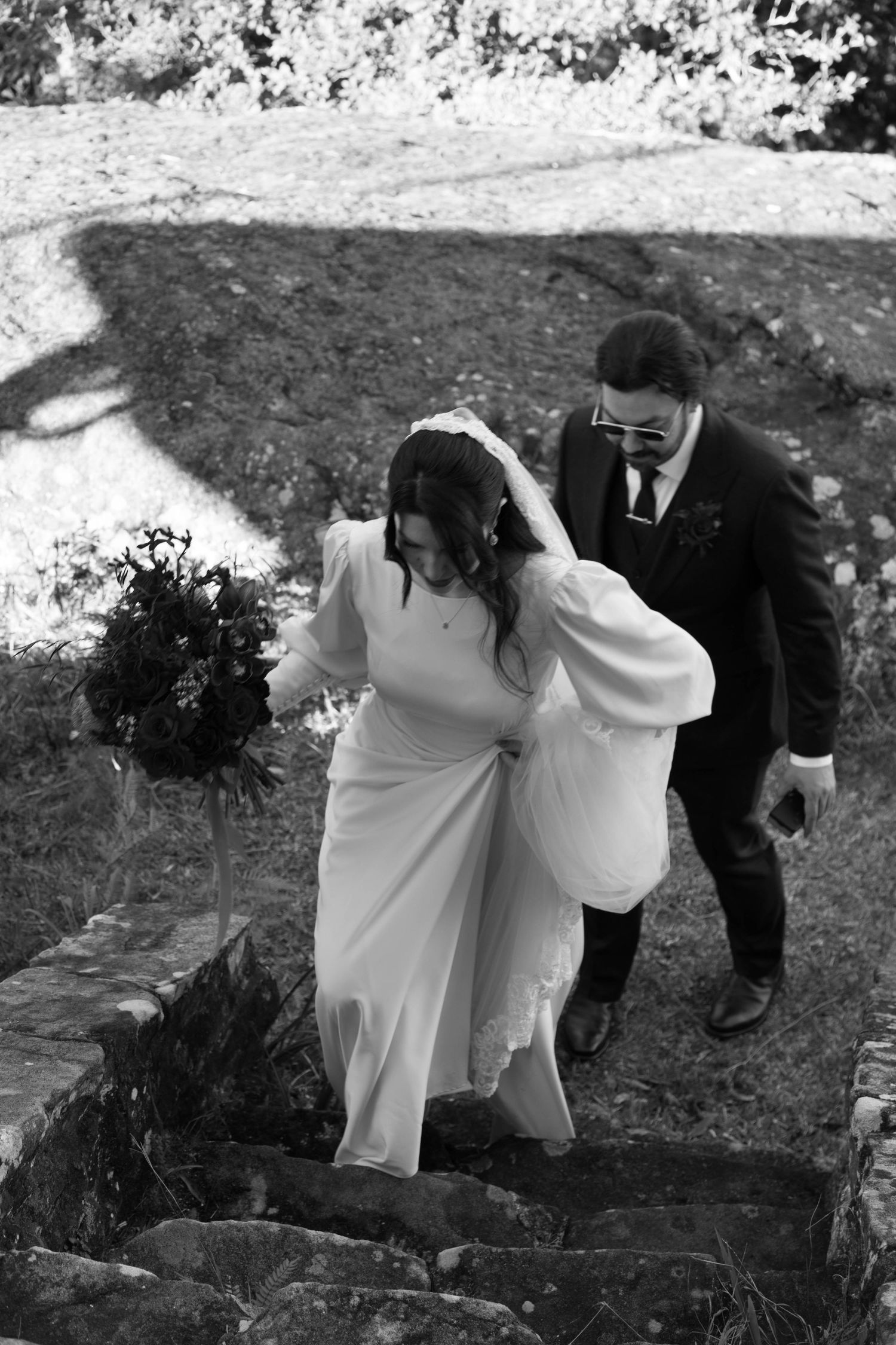 A couple carefully navigates stone steps outdoors during their wedding photoshoot.